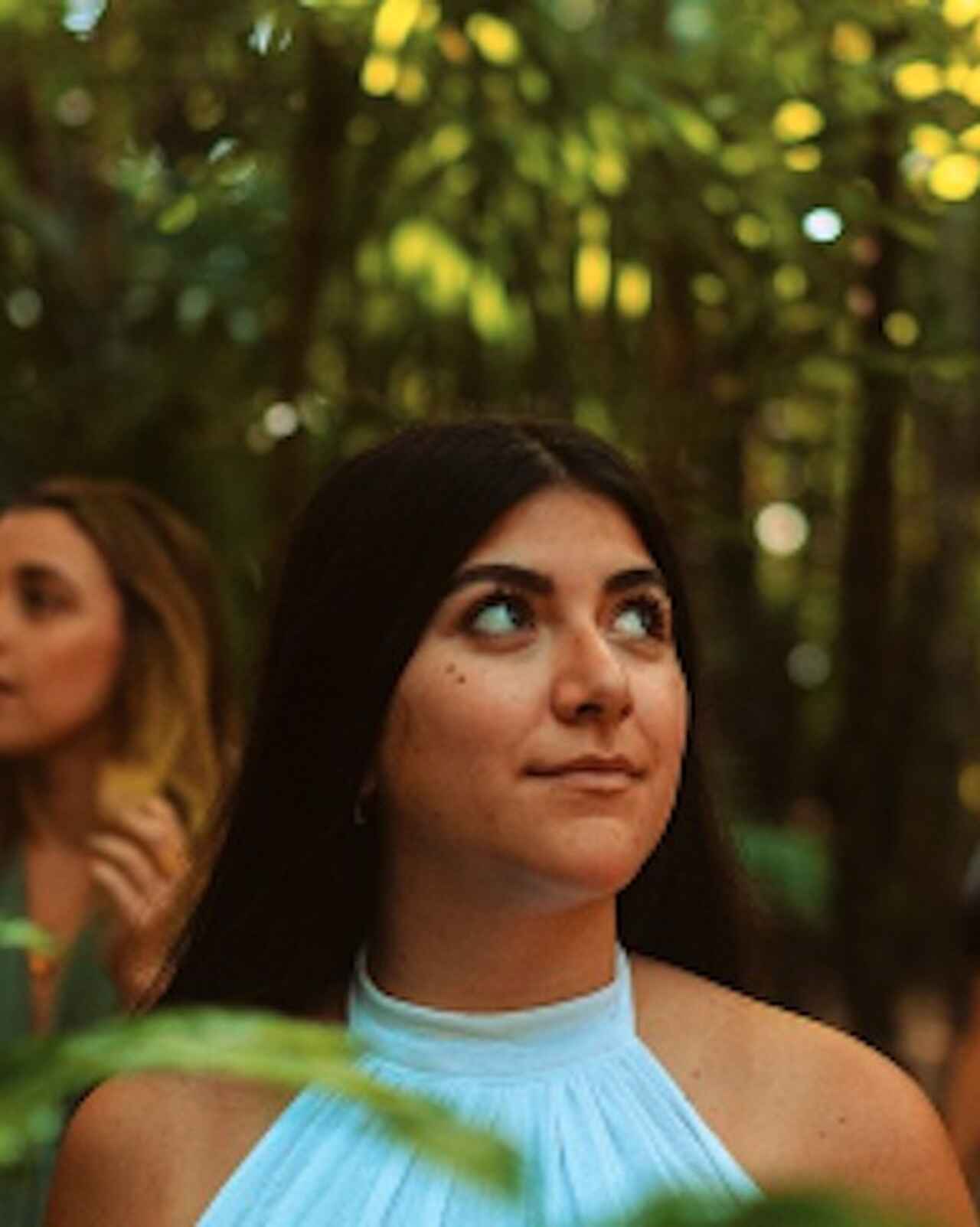 Mujer con top azul claro mirando hacia arriba en un entorno natural al aire libre