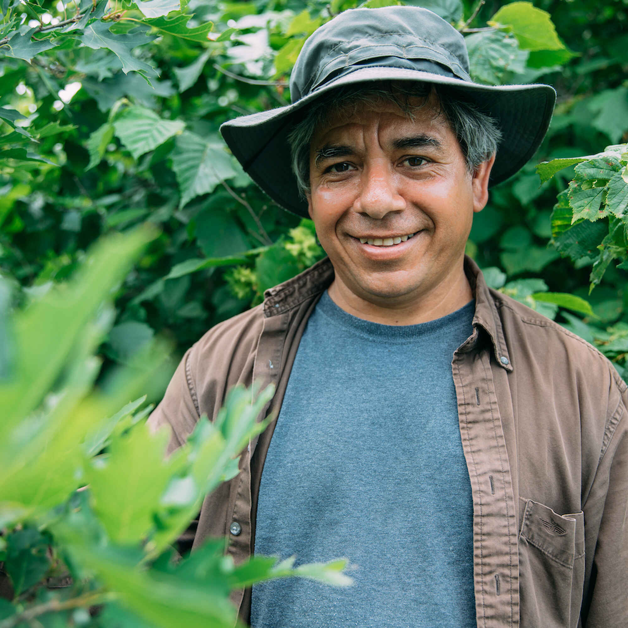 Reginaldo Haslett-Marroquin sonriendo entre plantas verdes en un huerto