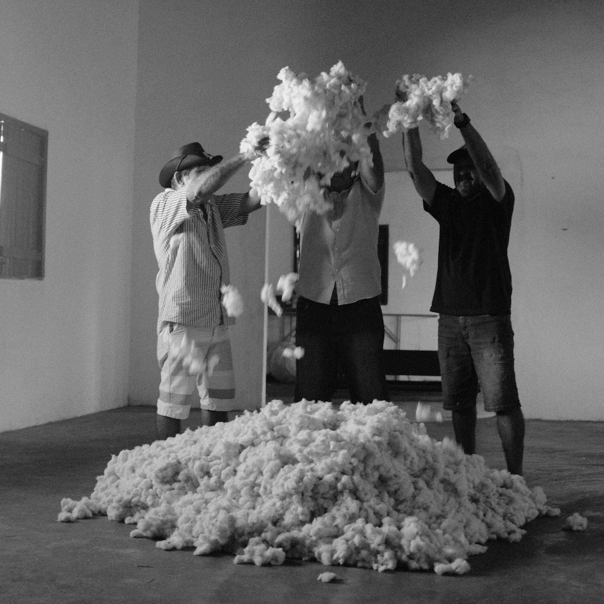 Three people toss white cotton or fiber into the air in an art gallery installation