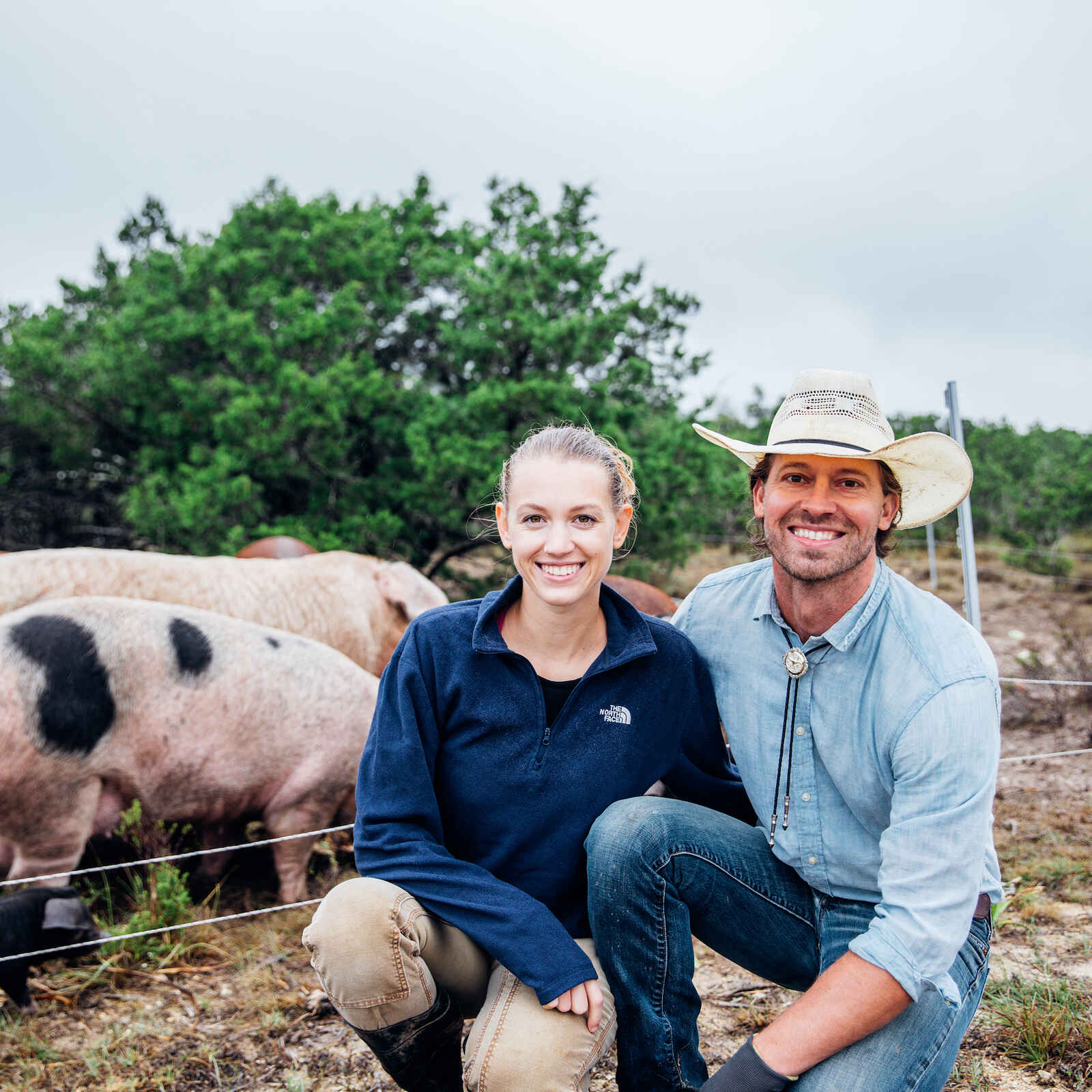 A man and woman crouch together in front of pigs on a ranch pasture