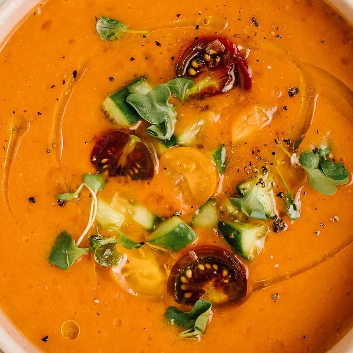 Taz&oacute;n de gazpacho naranja brillante cubierto con verduras cortadas en dados, rodajas de chile rojo y microverdes frescos