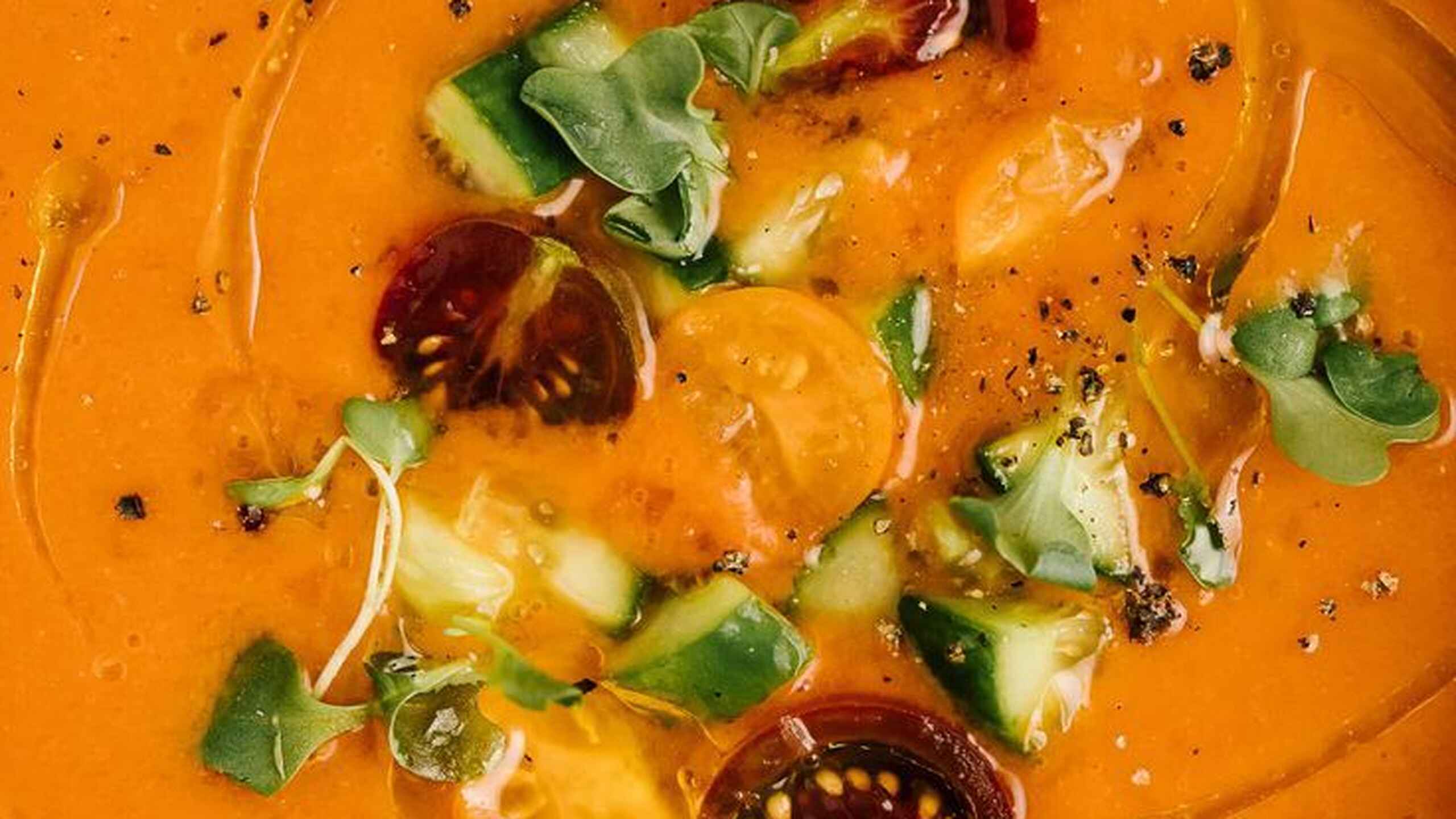 Taz&oacute;n de gazpacho naranja brillante cubierto con verduras cortadas en dados, rodajas de chile rojo y microverdes frescos