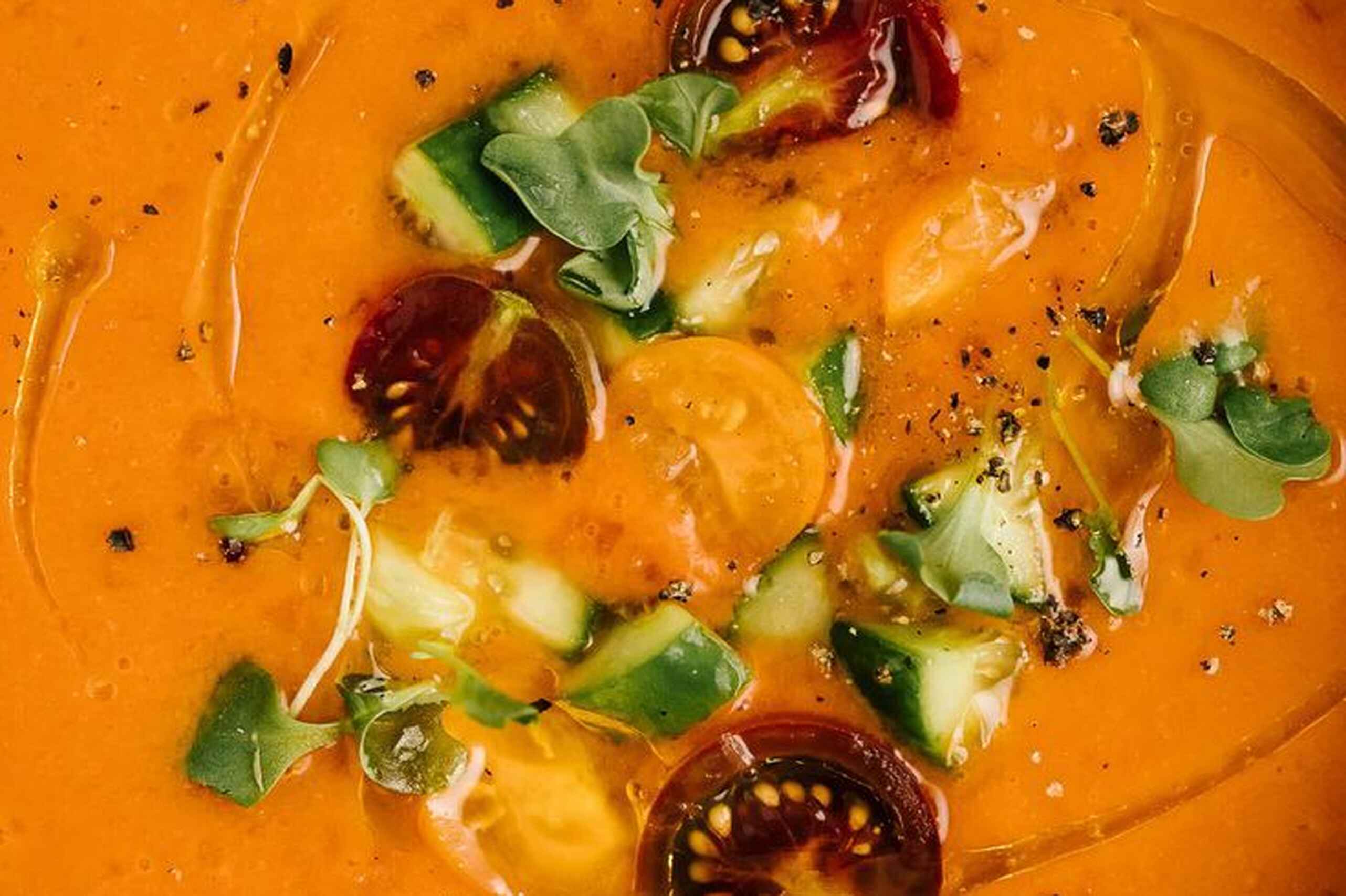 Taz&oacute;n de gazpacho naranja brillante cubierto con verduras cortadas en dados, rodajas de chile rojo y microverdes frescos