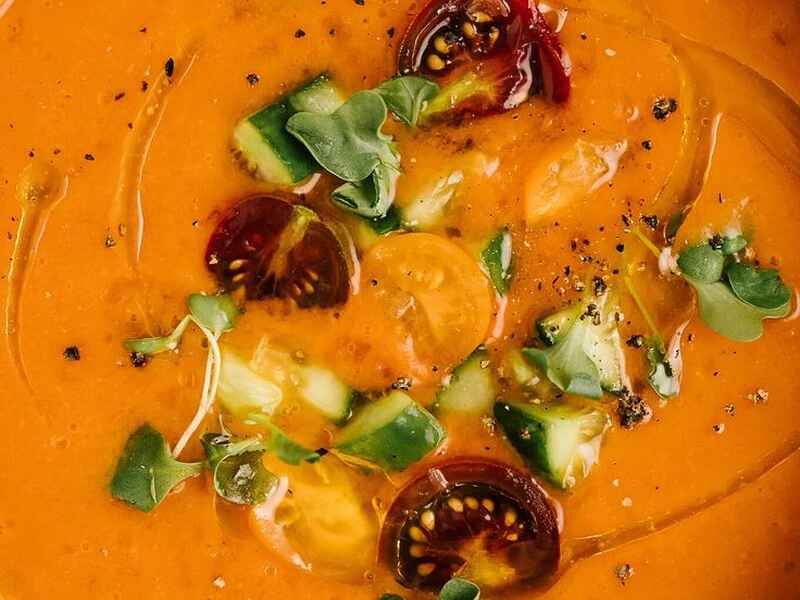 Taz&oacute;n de gazpacho naranja brillante cubierto con verduras cortadas en dados, rodajas de chile rojo y microverdes frescos
