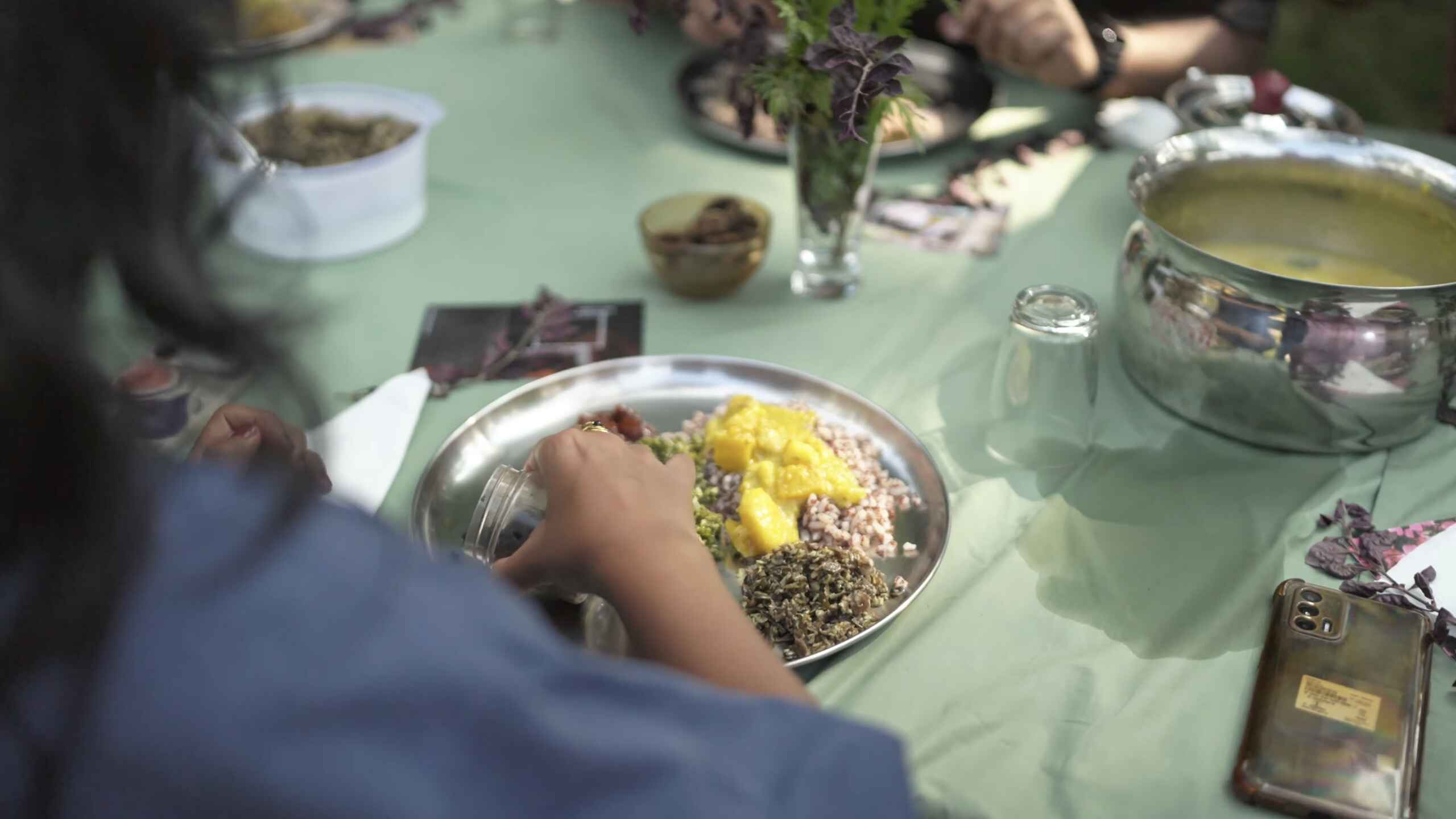 Person serving a plate of avial, a vegetable dish with yellow and green ingredients mixed with coconut