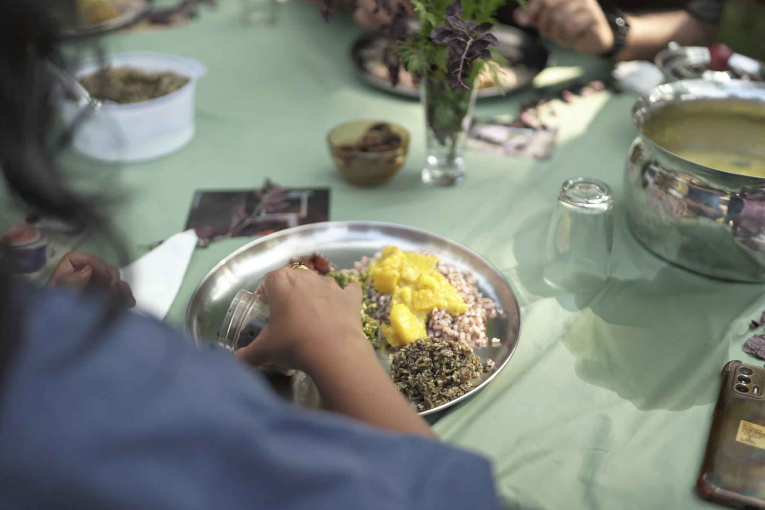 Person serving a plate of avial, a vegetable dish with yellow and green ingredients mixed with coconut