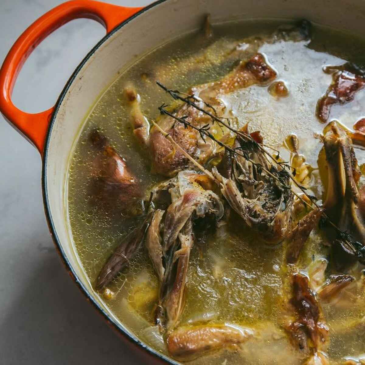 Caldo de huesos hirviendo a fuego lento en una olla holandesa con romero fresco y hierbas