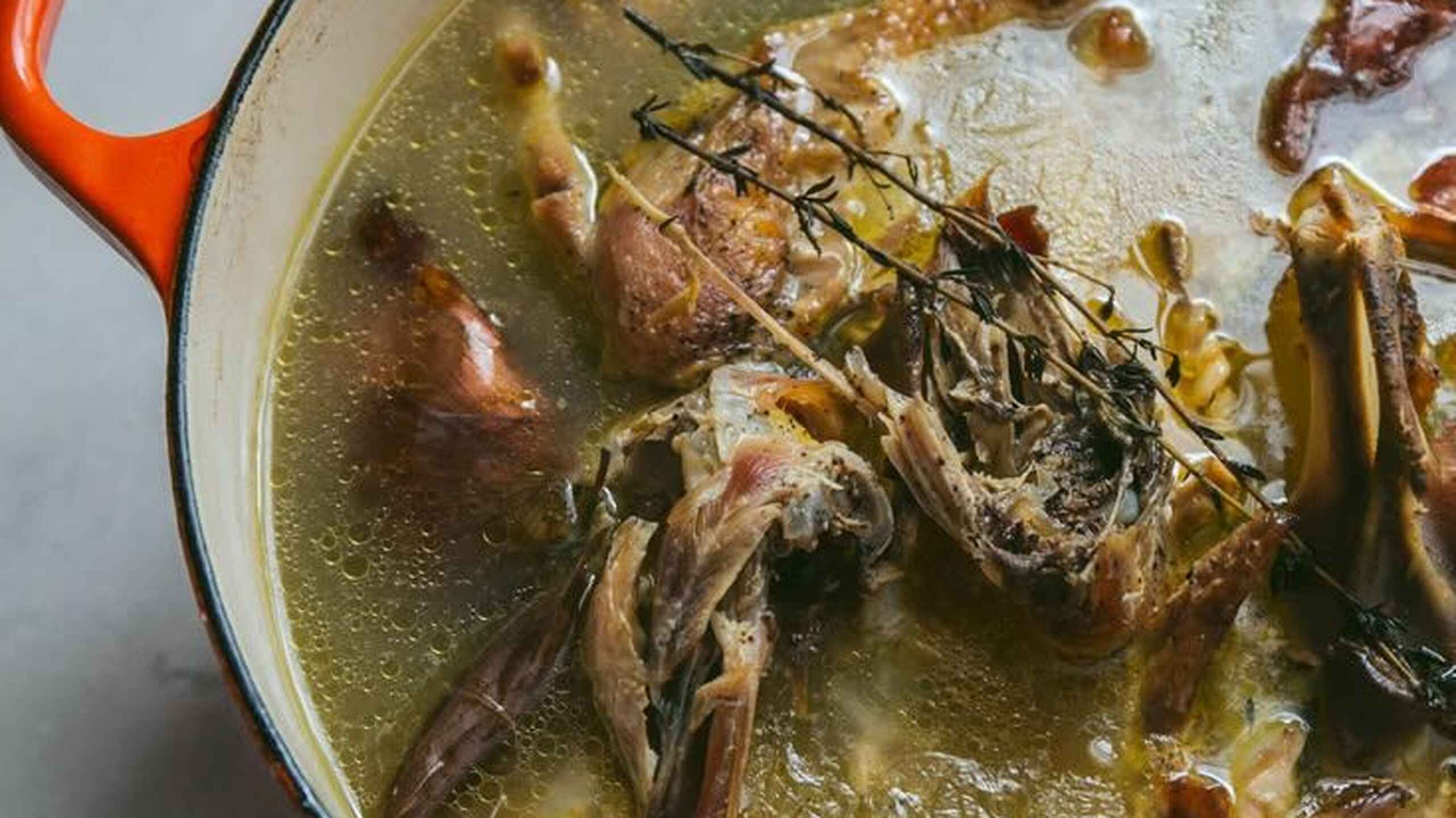 Caldo de huesos hirviendo a fuego lento en una olla holandesa con romero fresco y hierbas