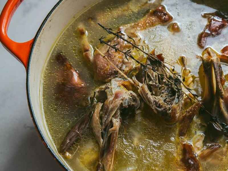 Bone broth simmering in a Dutch oven with fresh rosemary and herbs