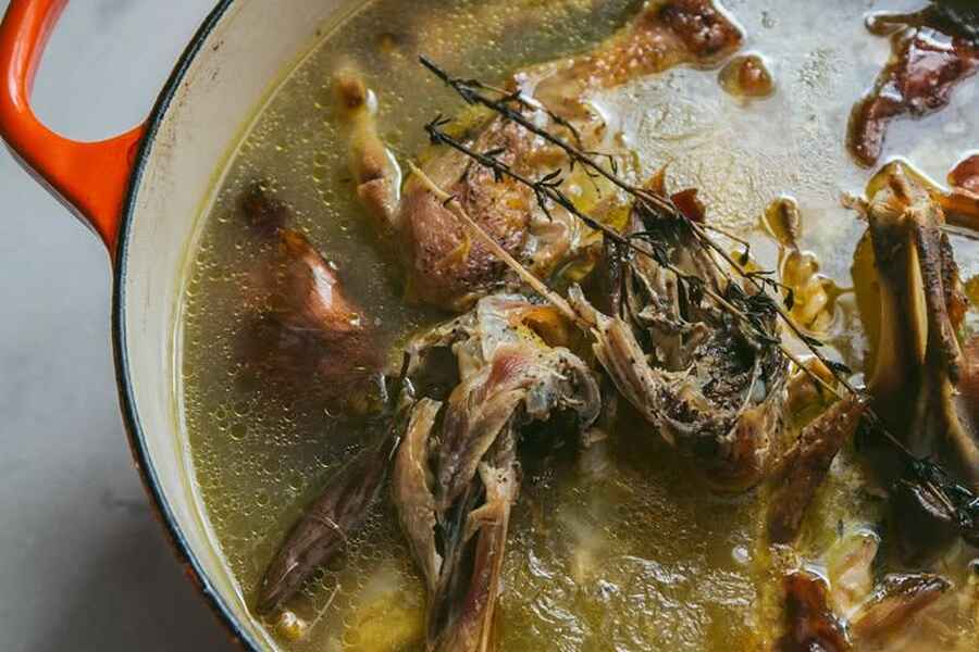 Bone broth simmering in a Dutch oven with fresh rosemary and herbs
