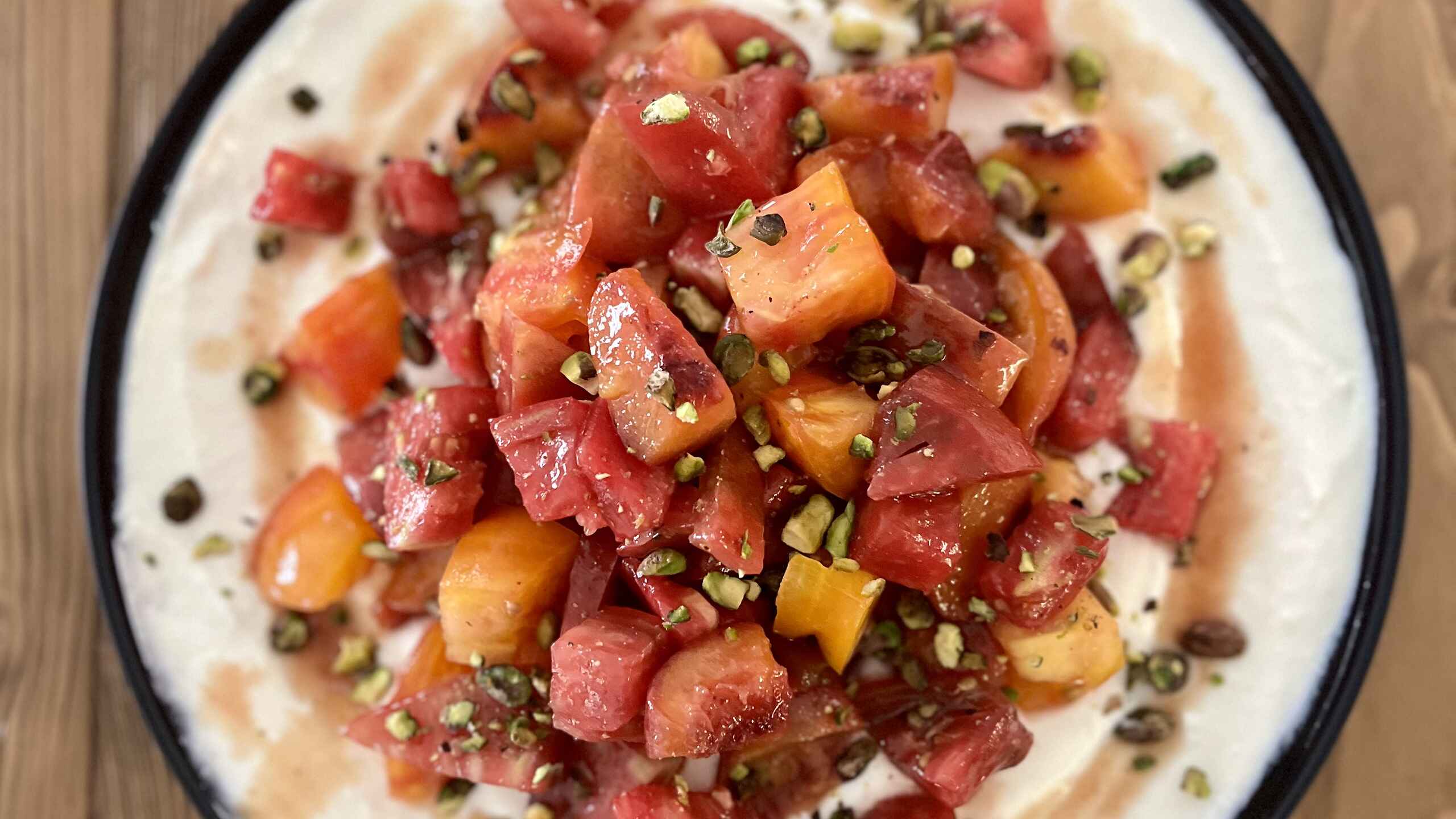 Caramelized Peach & Heirloom Tomato Salad on Whipped Feta garnished with pistachios and served on a plate with black rim