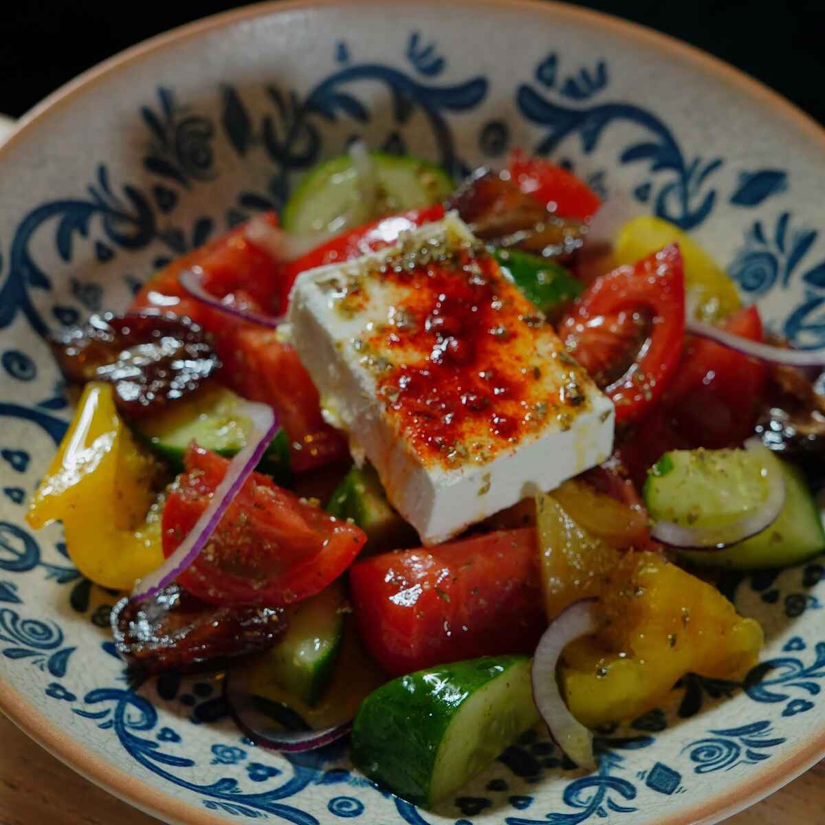 Greek salad with feta cheese, tomatoes, cucumbers, bell peppers, and red onions on a decorative blue and white plate
