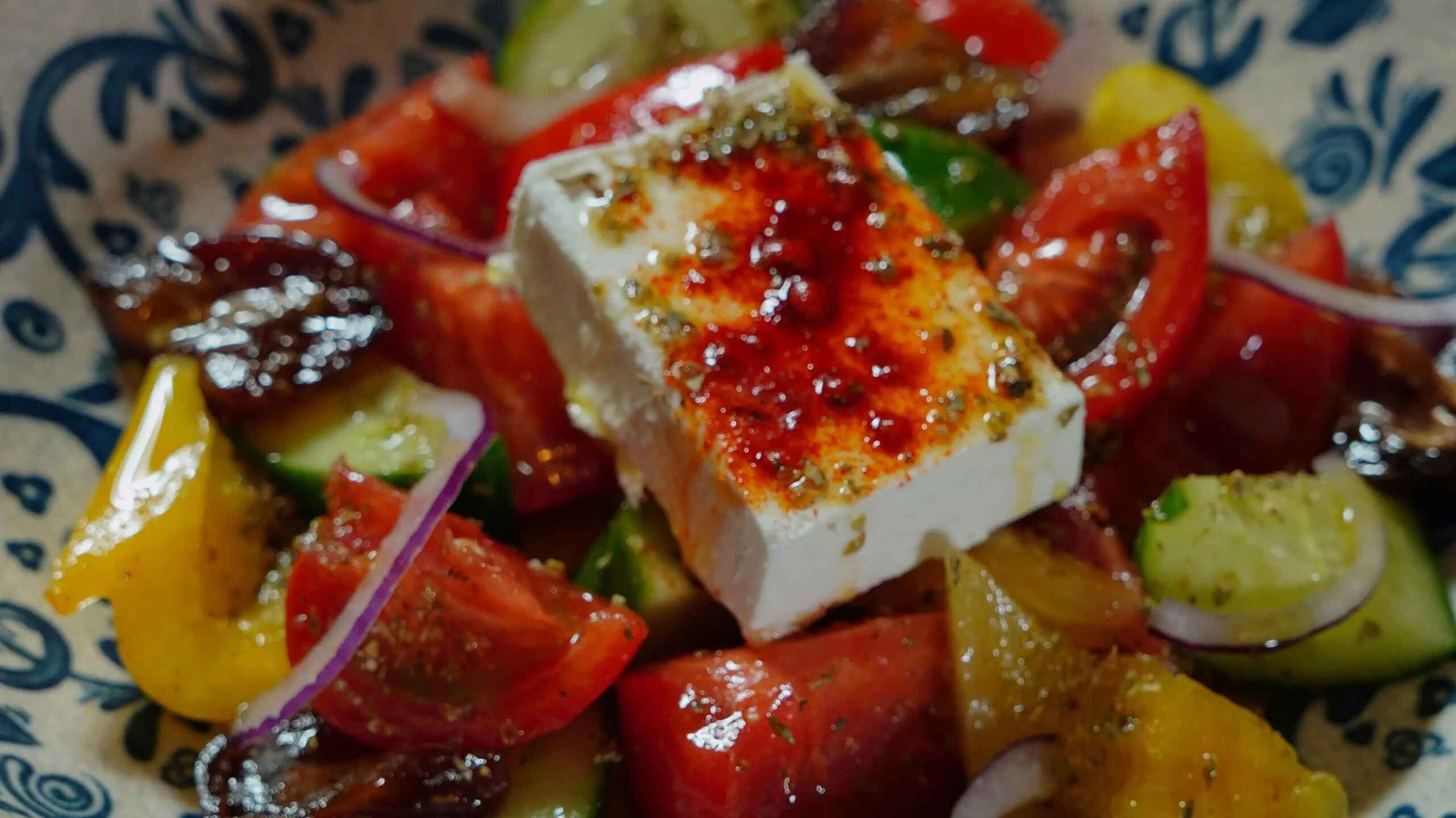 Greek salad with feta cheese, tomatoes, cucumbers, bell peppers, and red onions on a decorative blue and white plate