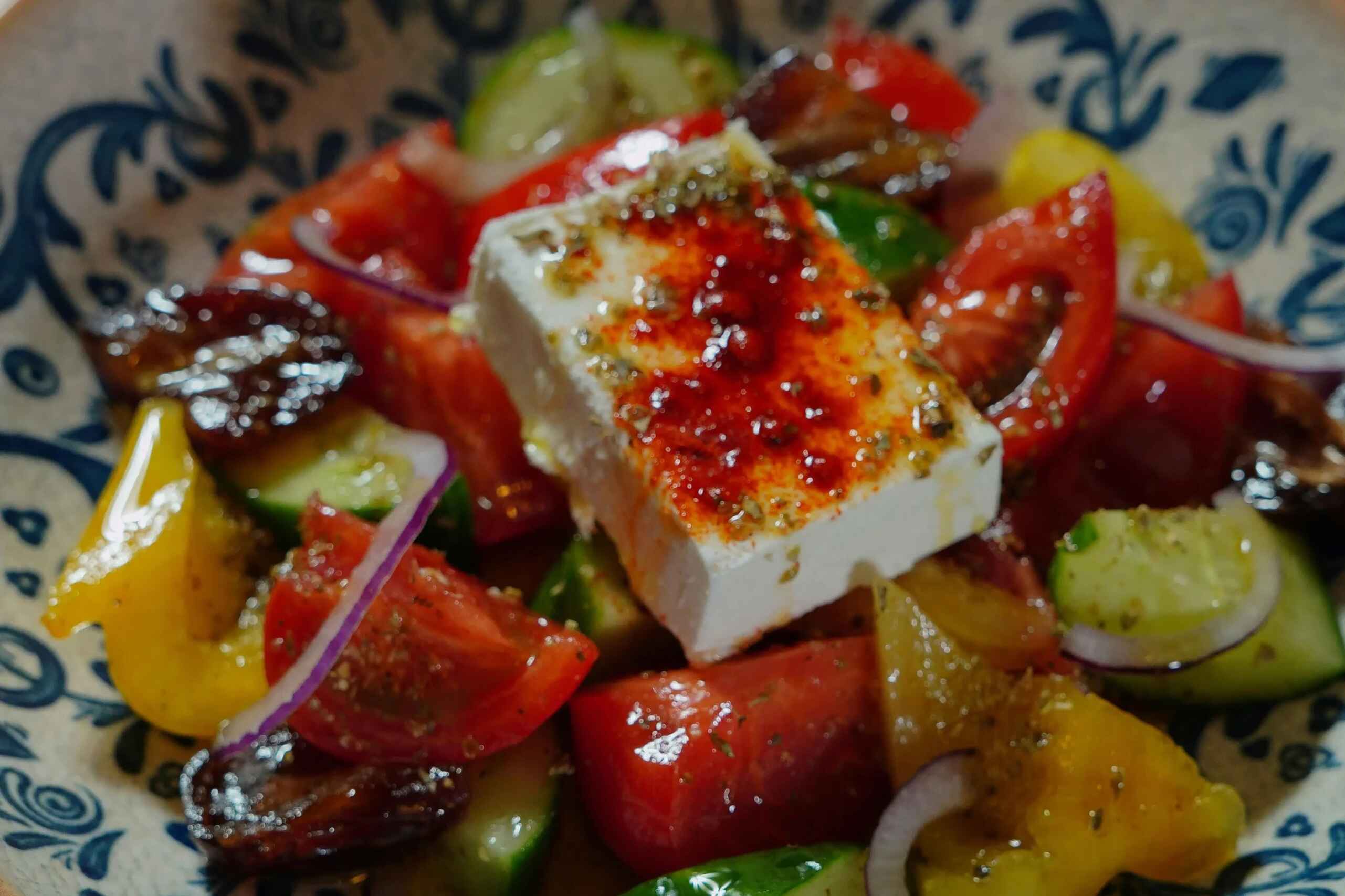 Greek salad with feta cheese, tomatoes, cucumbers, bell peppers, and red onions on a decorative blue and white plate