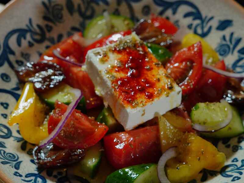 Ensalada griega con queso feta, tomates, pepinos, pimientos y cebolla morada en un plato decorativo azul y blanco