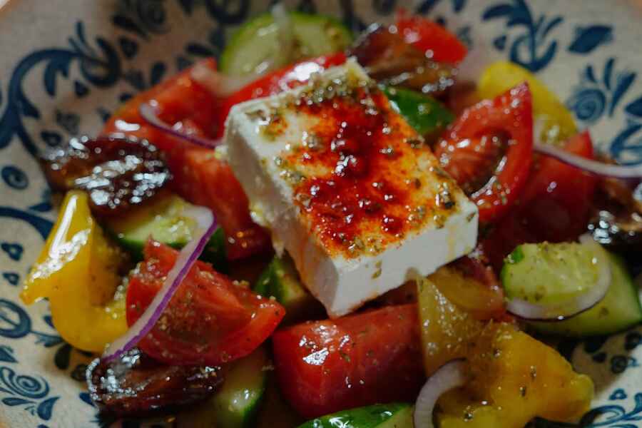 Greek salad with feta cheese, tomatoes, cucumbers, bell peppers, and red onions on a decorative blue and white plate