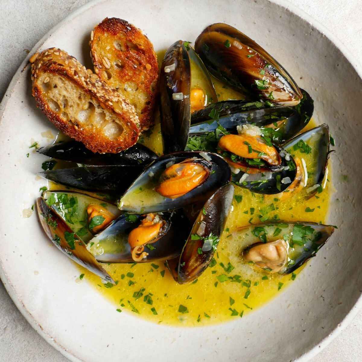 Steamed mussels in saffron broth with charred bread on a white plate