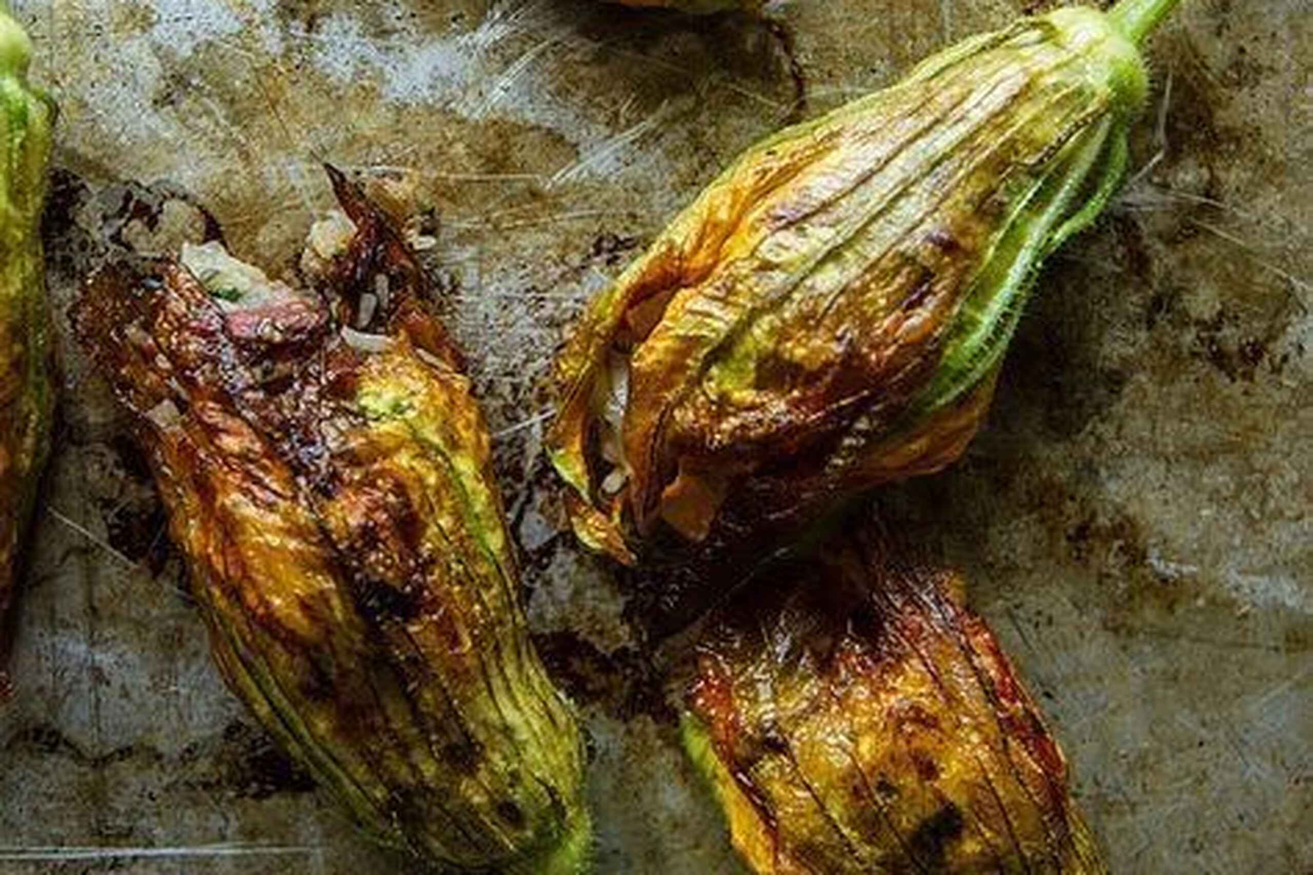 Flores de calabaza salteadas con p&eacute;talos dorados en una superficie met&aacute;lica r&uacute;stica