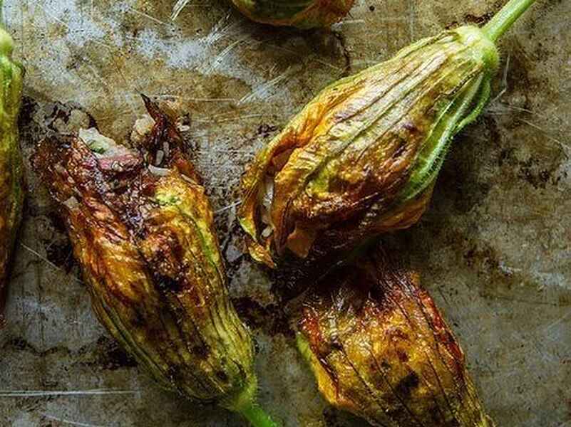 Flores de calabaza salteadas con p&eacute;talos dorados en una superficie met&aacute;lica r&uacute;stica