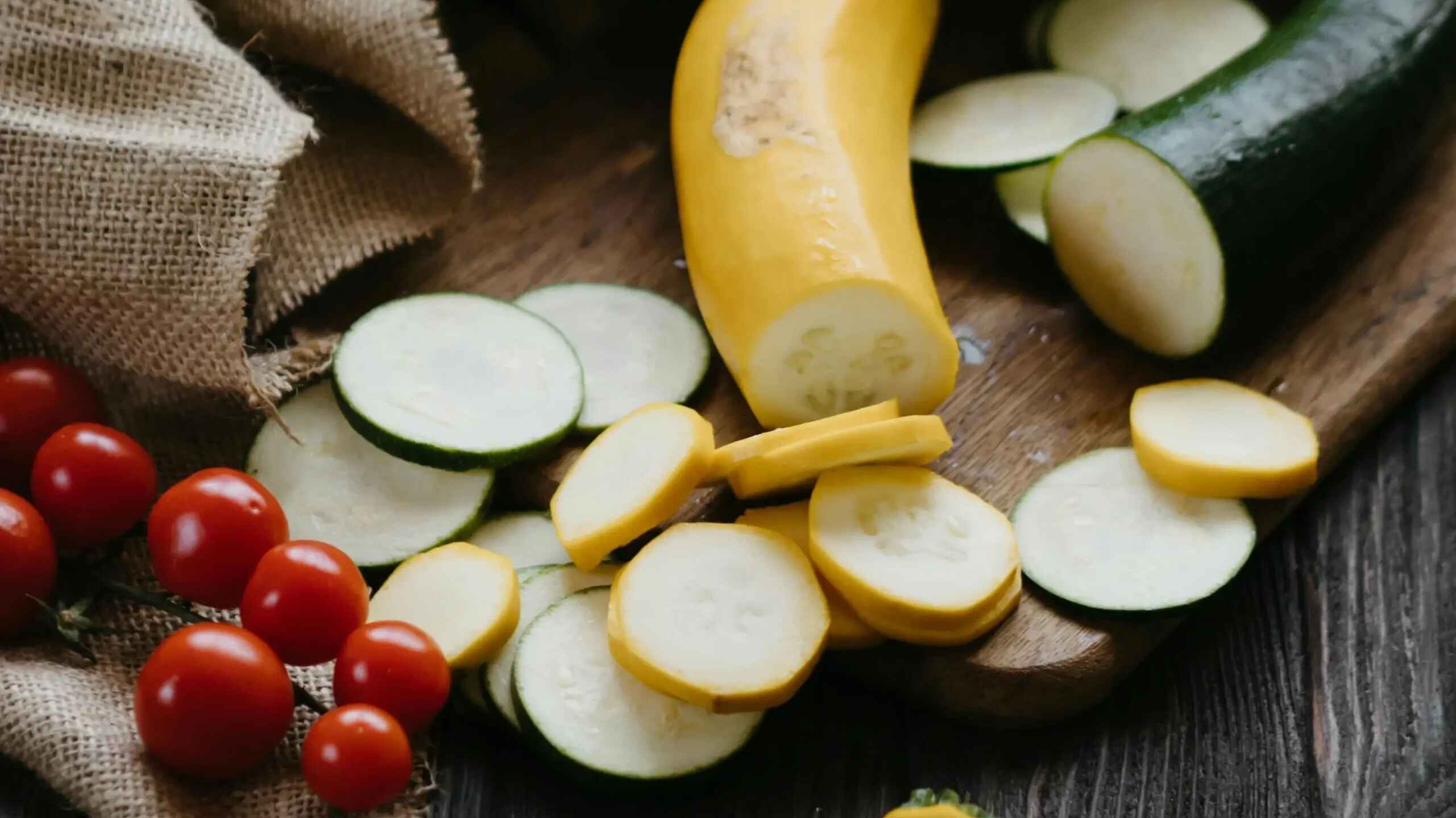 Fresh yellow squash and zucchini sliced on a wooden surface with cherry tomatoes and lettuce for preparing calabacita tacos