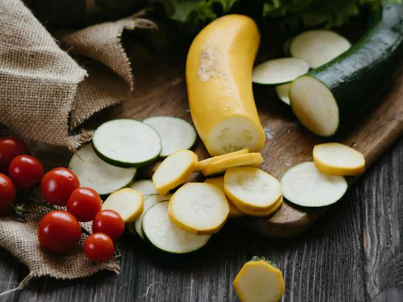 Fresh yellow squash and zucchini sliced on a wooden surface with cherry tomatoes and lettuce for preparing calabacita tacos
