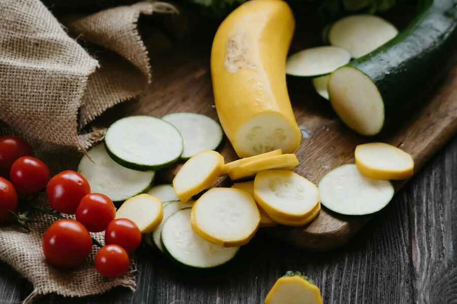 Fresh yellow squash and zucchini sliced on a wooden surface with cherry tomatoes and lettuce for preparing calabacita tacos