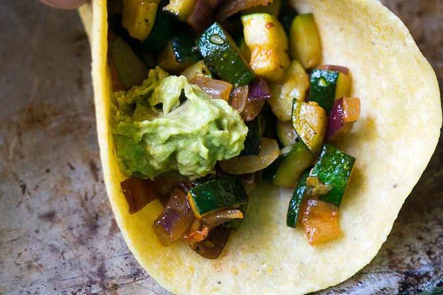 Vegetarian tacos filled with saut&eacute;ed zucchini, peppers, and guacamole on a corn tortilla