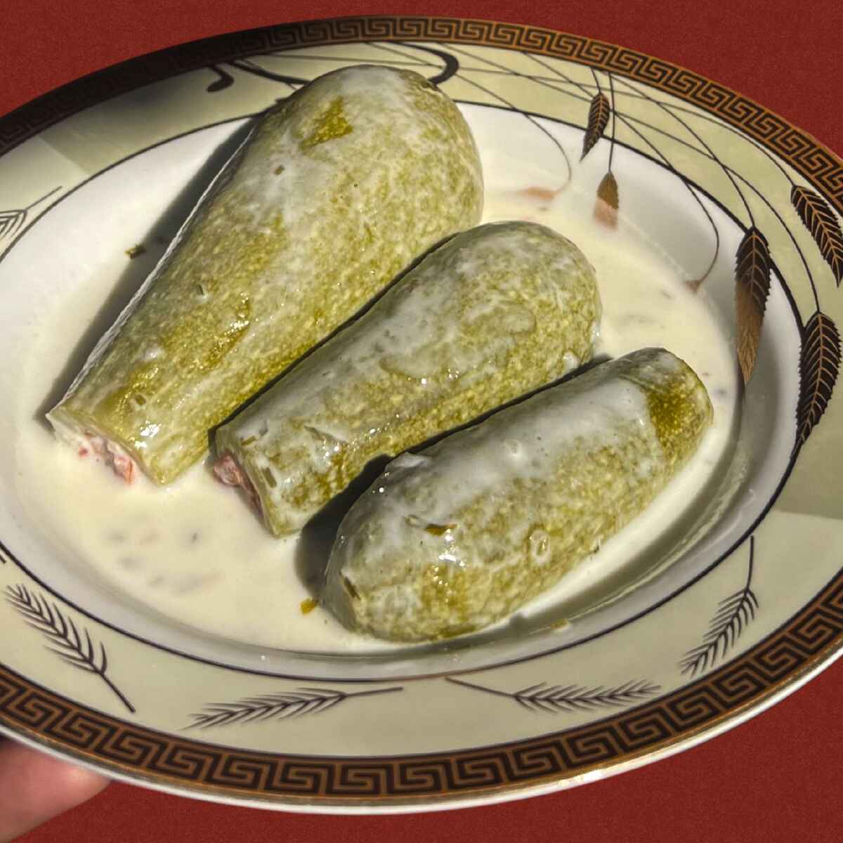 Three dolmas filled with herbs and rice served in a creamy yogurt sauce on a decorative plate