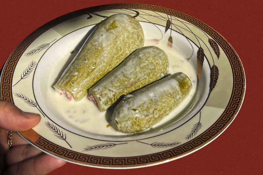 Three dolmas filled with herbs and rice served in a creamy yogurt sauce on a decorative plate