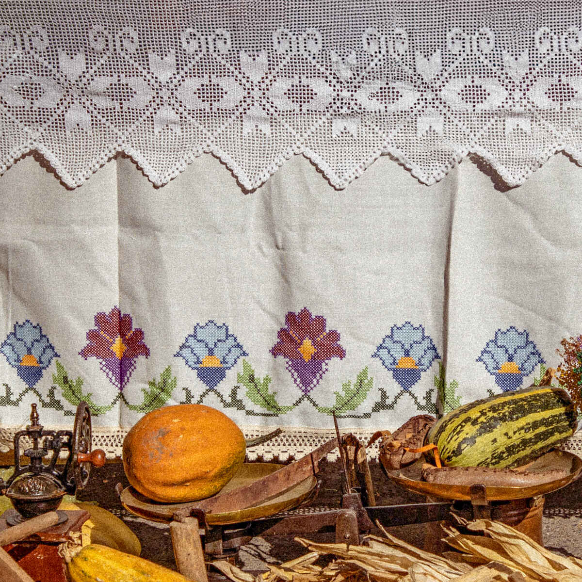 Traditional embroidered cloth backdrop with heirloom vegetables including corn, squash, and beans arranged on a rustic display