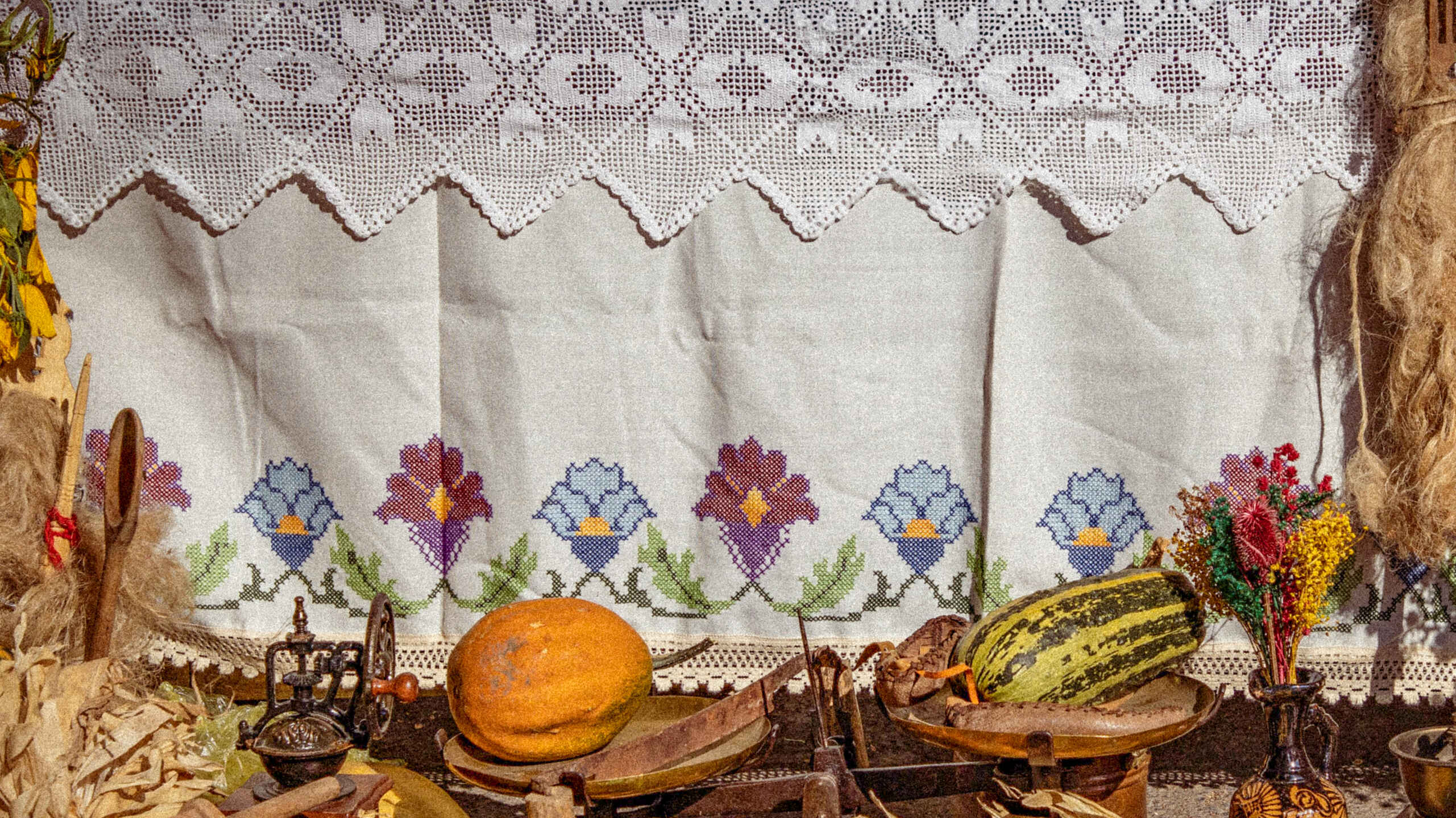 Traditional embroidered cloth backdrop with heirloom vegetables including corn, squash, and beans arranged on a rustic display