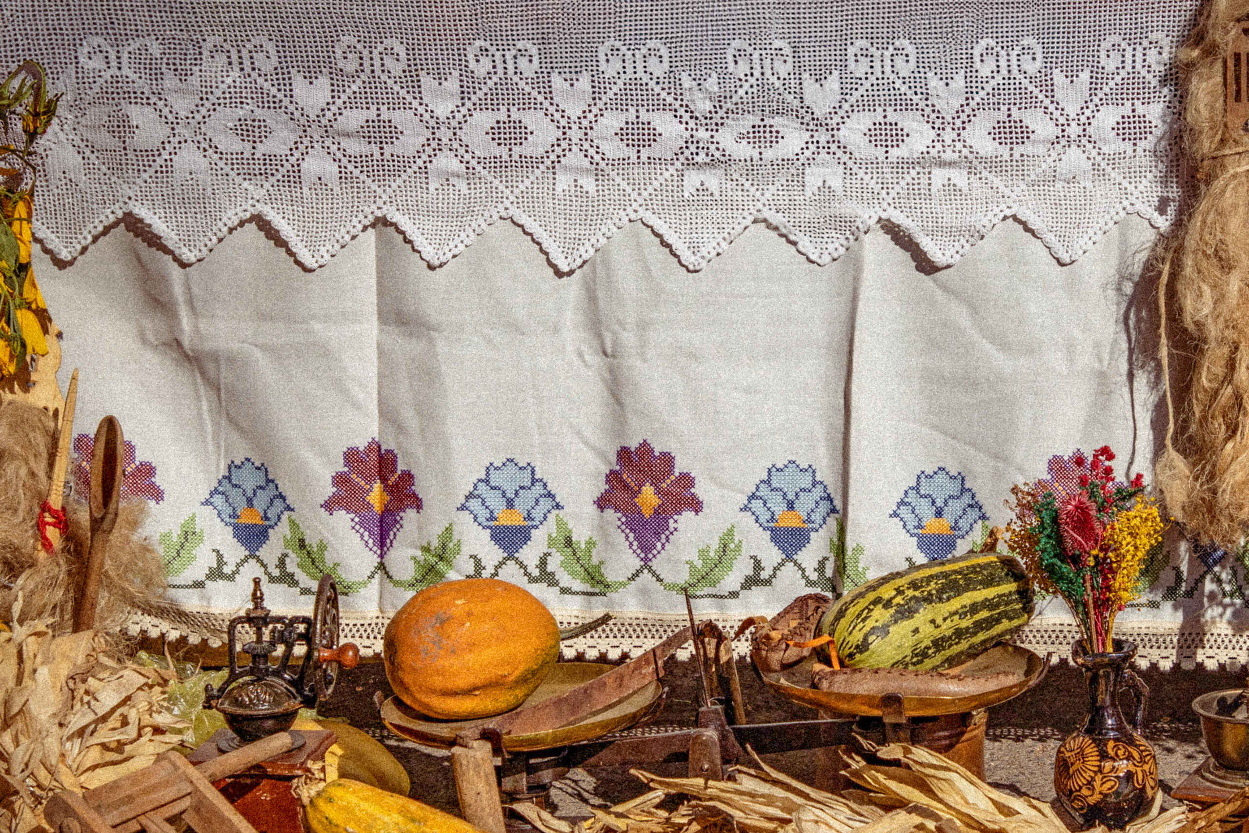 Traditional embroidered cloth backdrop with heirloom vegetables including corn, squash, and beans arranged on a rustic display