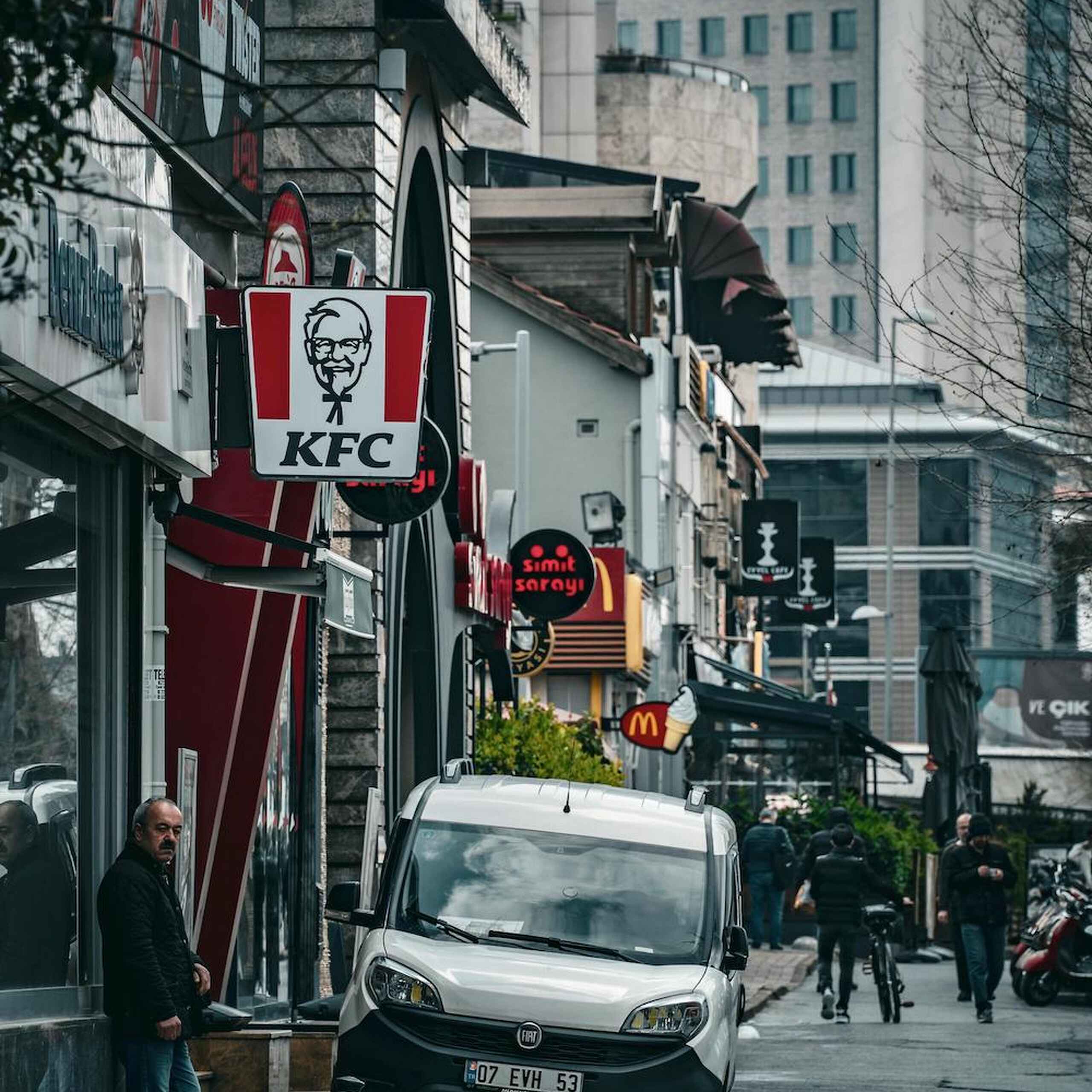 Urban street with KFC and McDonald's signs among tall buildings and pedestrians