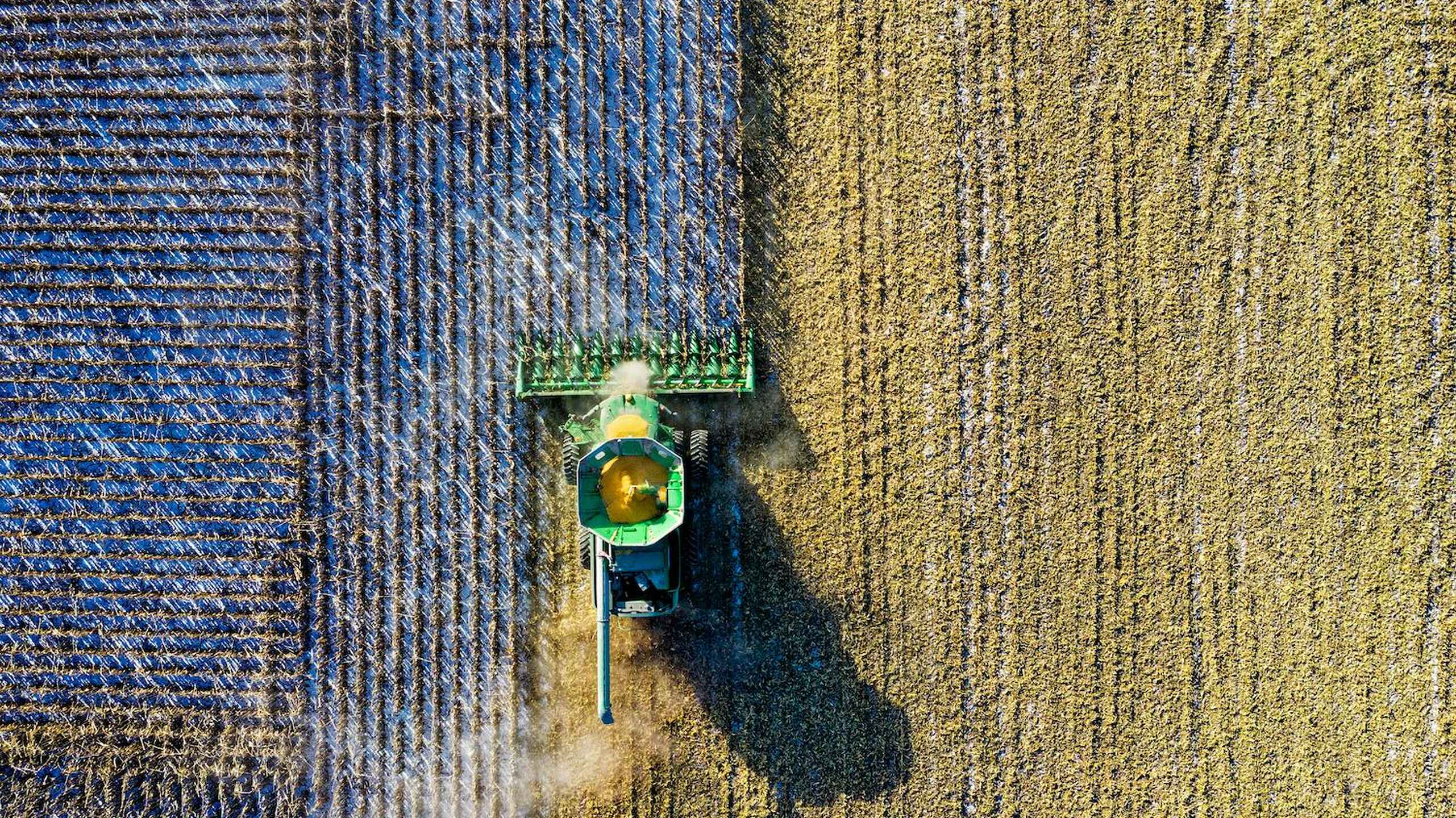 Aerial view of a combine harvester working across fields of different crops