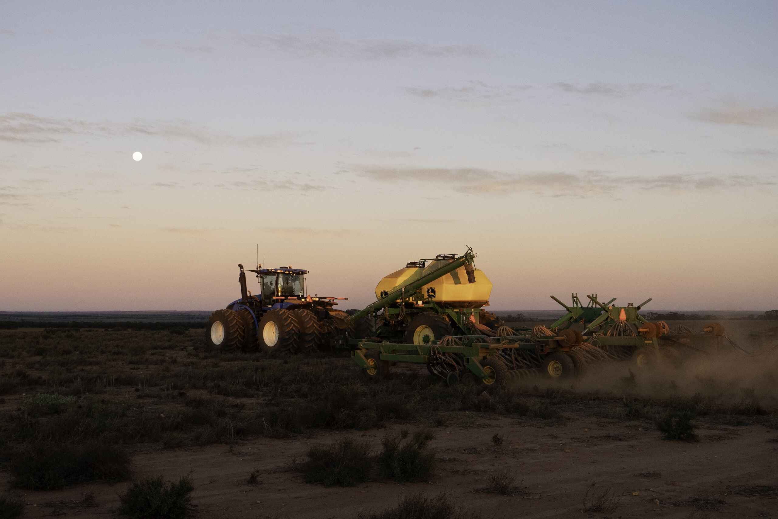 Large tractor pulling agricultural equipment across dusty farmland at dusk