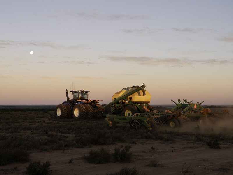Tractor grande tirando equipo agr&iacute;cola a trav&eacute;s de tierra de cultivo polvoriento al atardecer