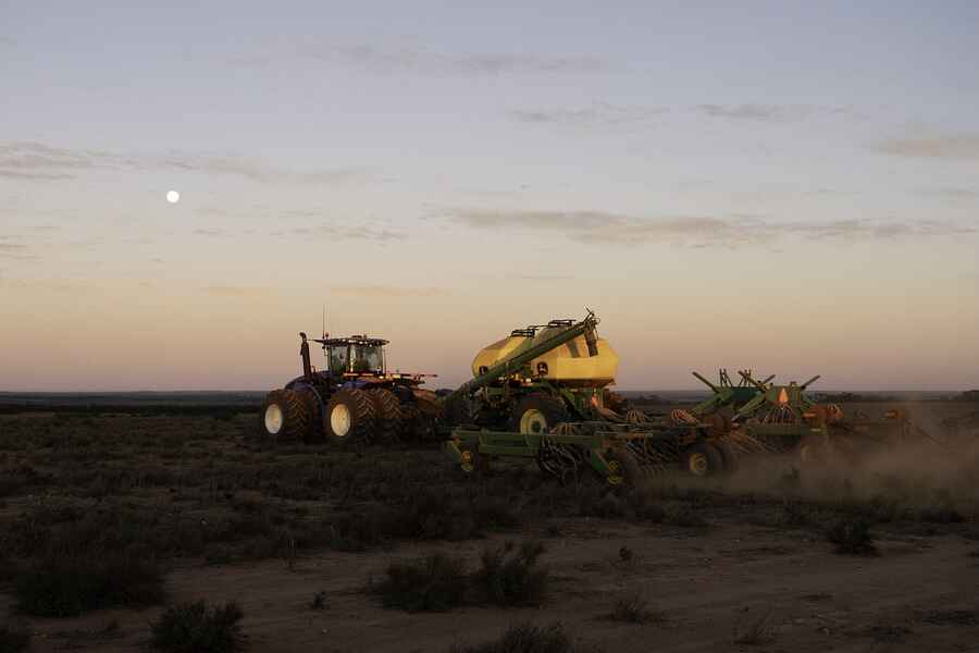 Tractor grande tirando equipo agr&iacute;cola a trav&eacute;s de tierra de cultivo polvoriento al atardecer