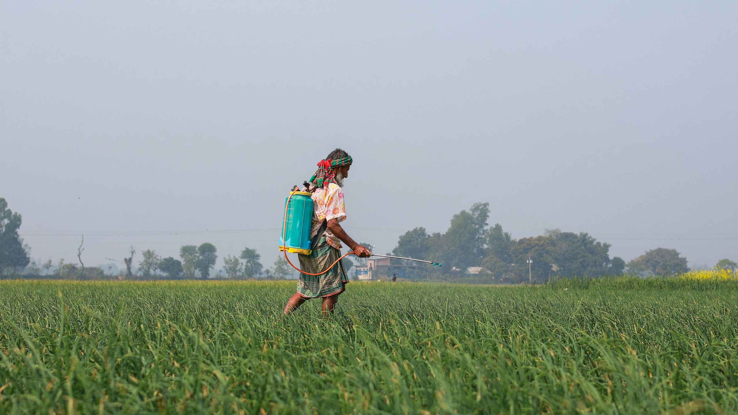 Farmer spraying pesticides across a green crop field