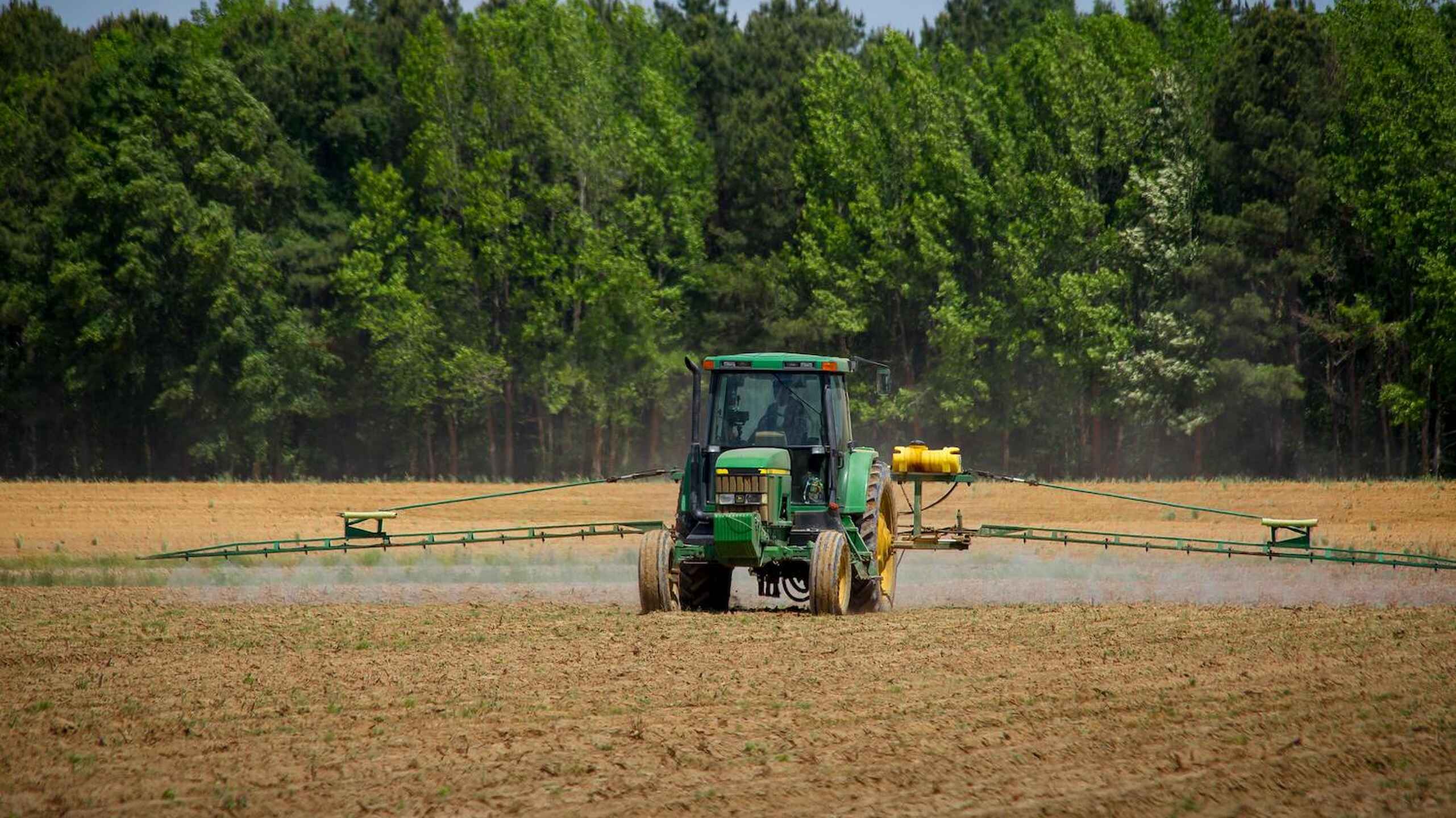 Green tractor with spray boom applying pesticides across a farm field