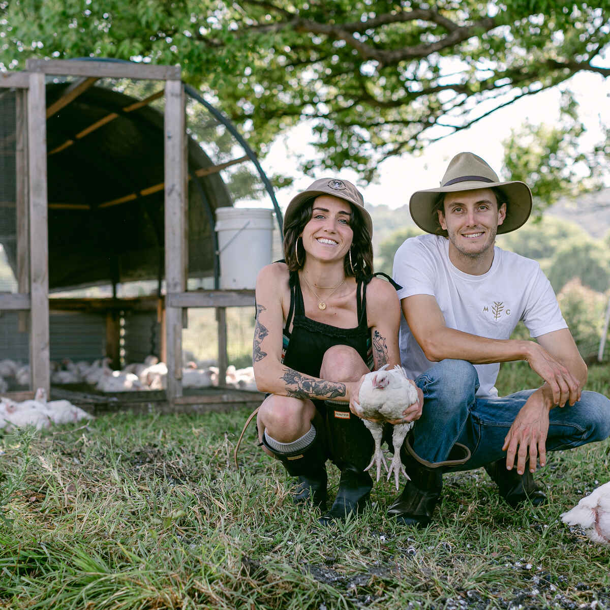 Two farmers holding a chicken in front of a mobile coop at their agroforestry farm