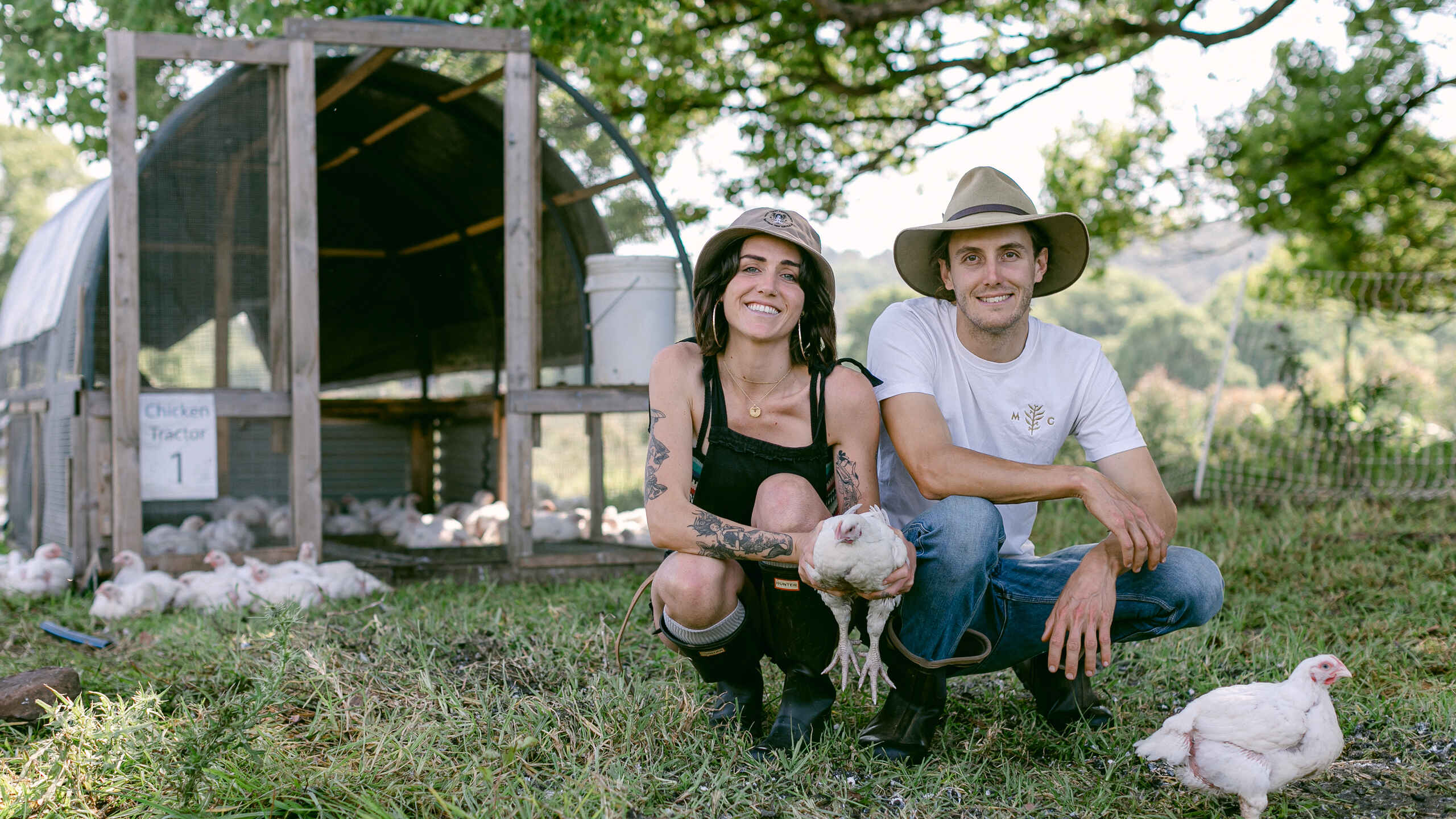 Two farmers holding a chicken in front of a mobile coop at their agroforestry farm