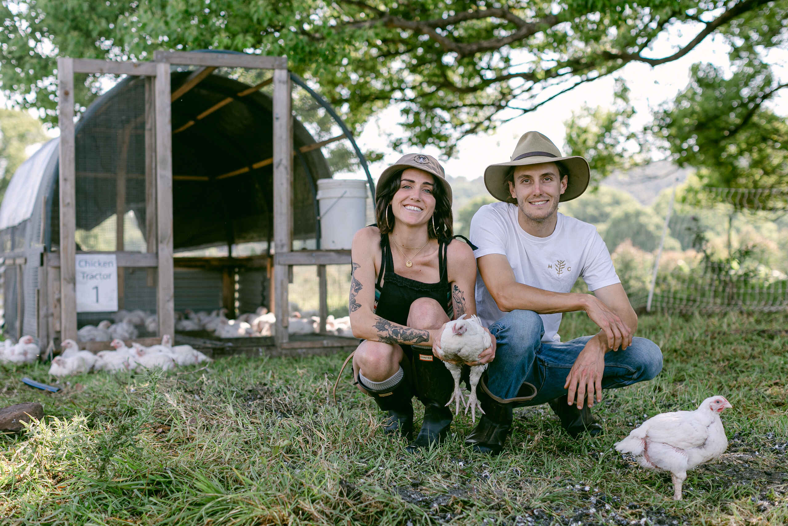 Two farmers holding a chicken in front of a mobile coop at their agroforestry farm