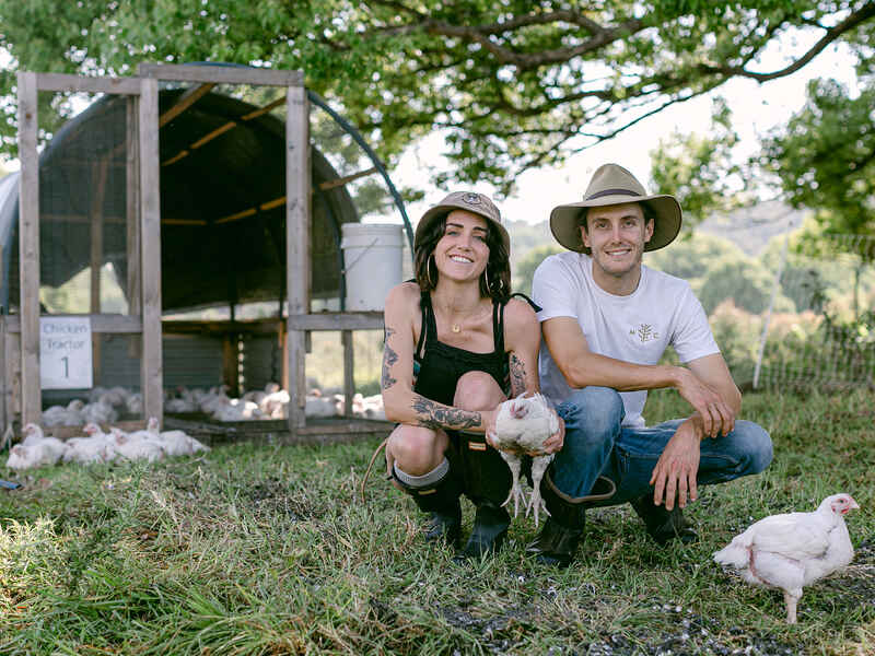 Dos agricultores sosteniendo un pollo frente a un gallinero m&oacute;vil en su granja agroforestal