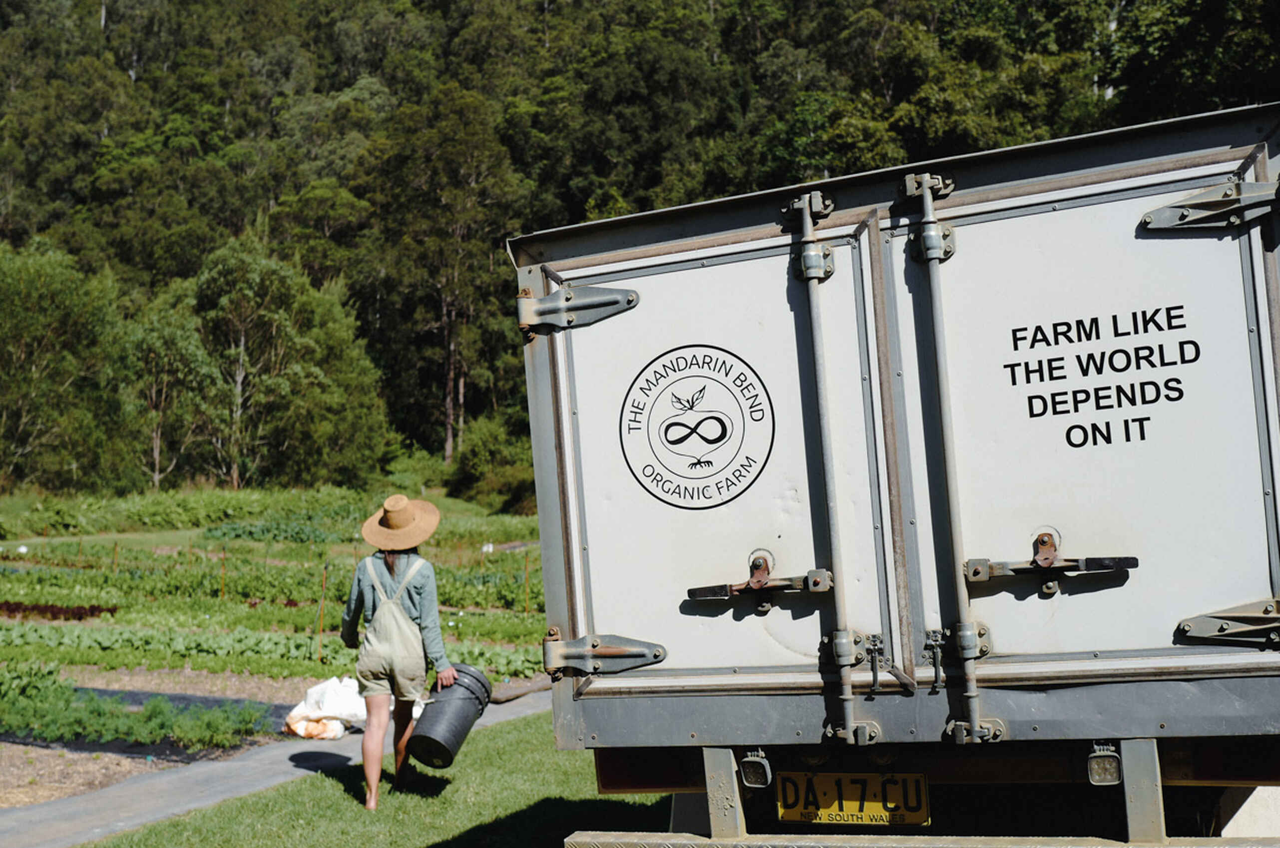 Farmer walking toward The Mandarin Farm organic farm truck with the message "Farm Like The World Depends On It"