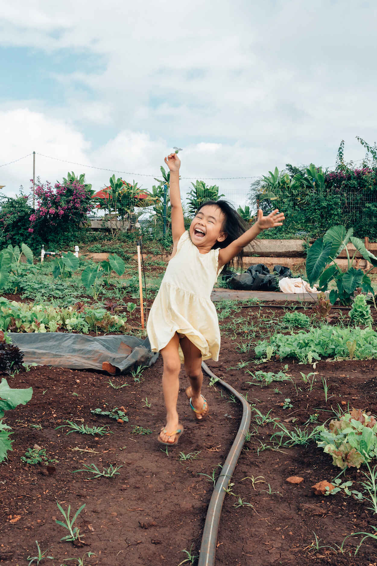 Child celebrating in a vegetable garden with a red farmhouse in the background