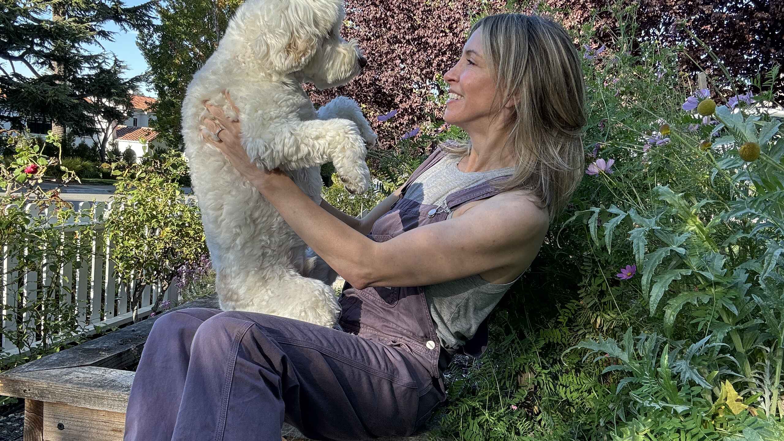 Woman holding a small white dog in a garden setting
