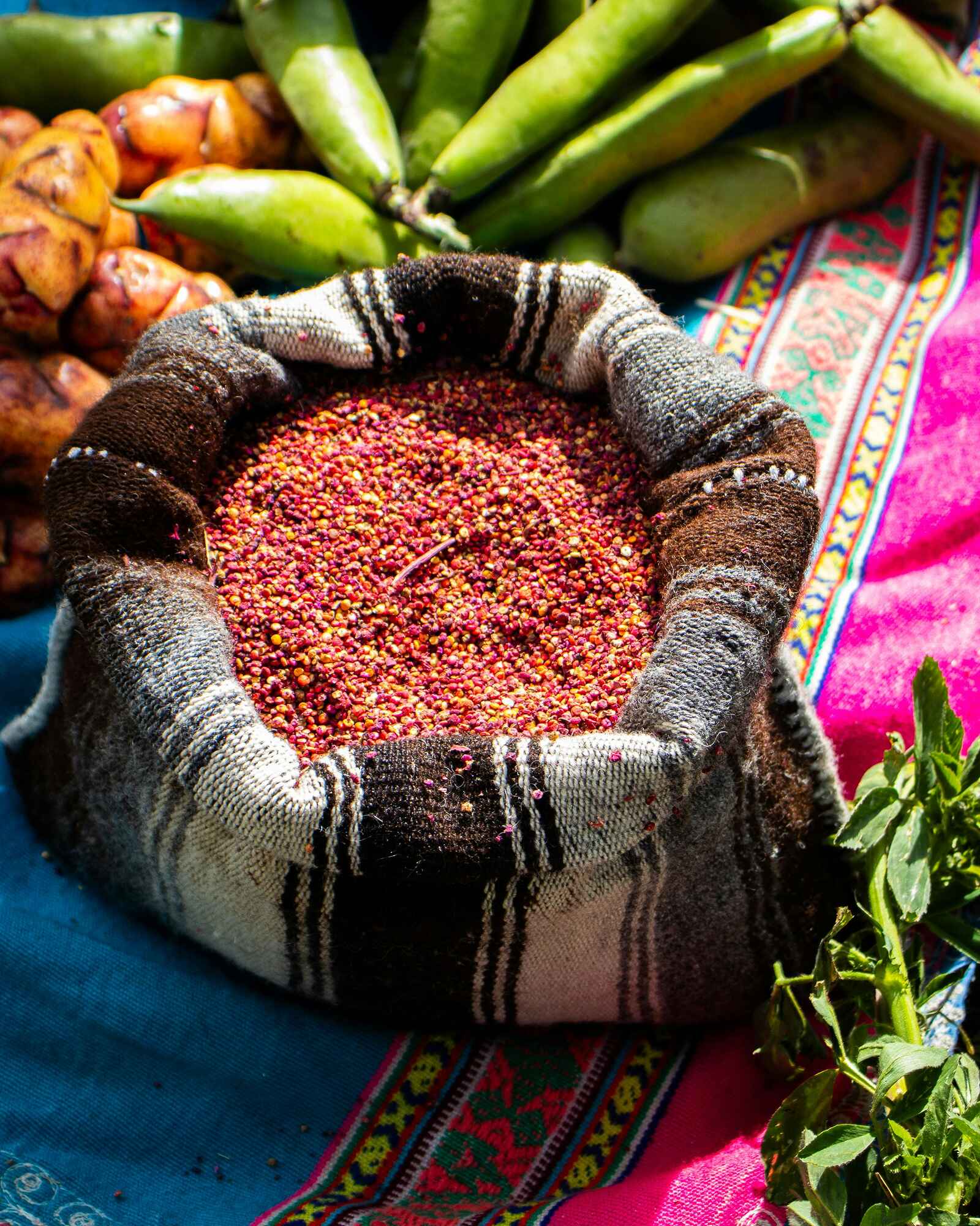 Quinoa seeds in a traditional cloth with fresh produce and herbs displayed on colorful woven textiles