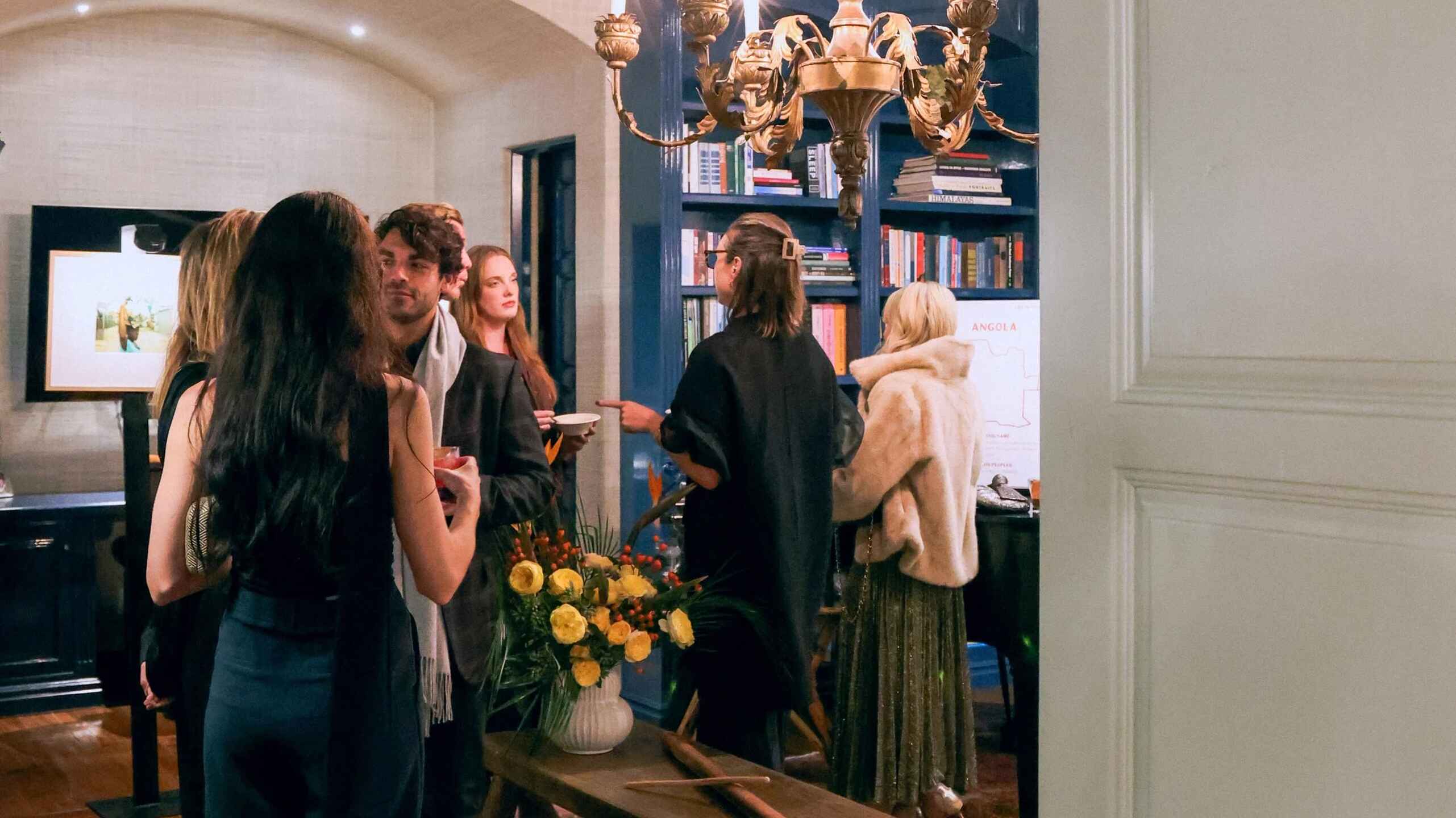 Group of people gathered in an elegant interior space with a brass chandelier and blue coffered ceiling, engaged in conversation during an event