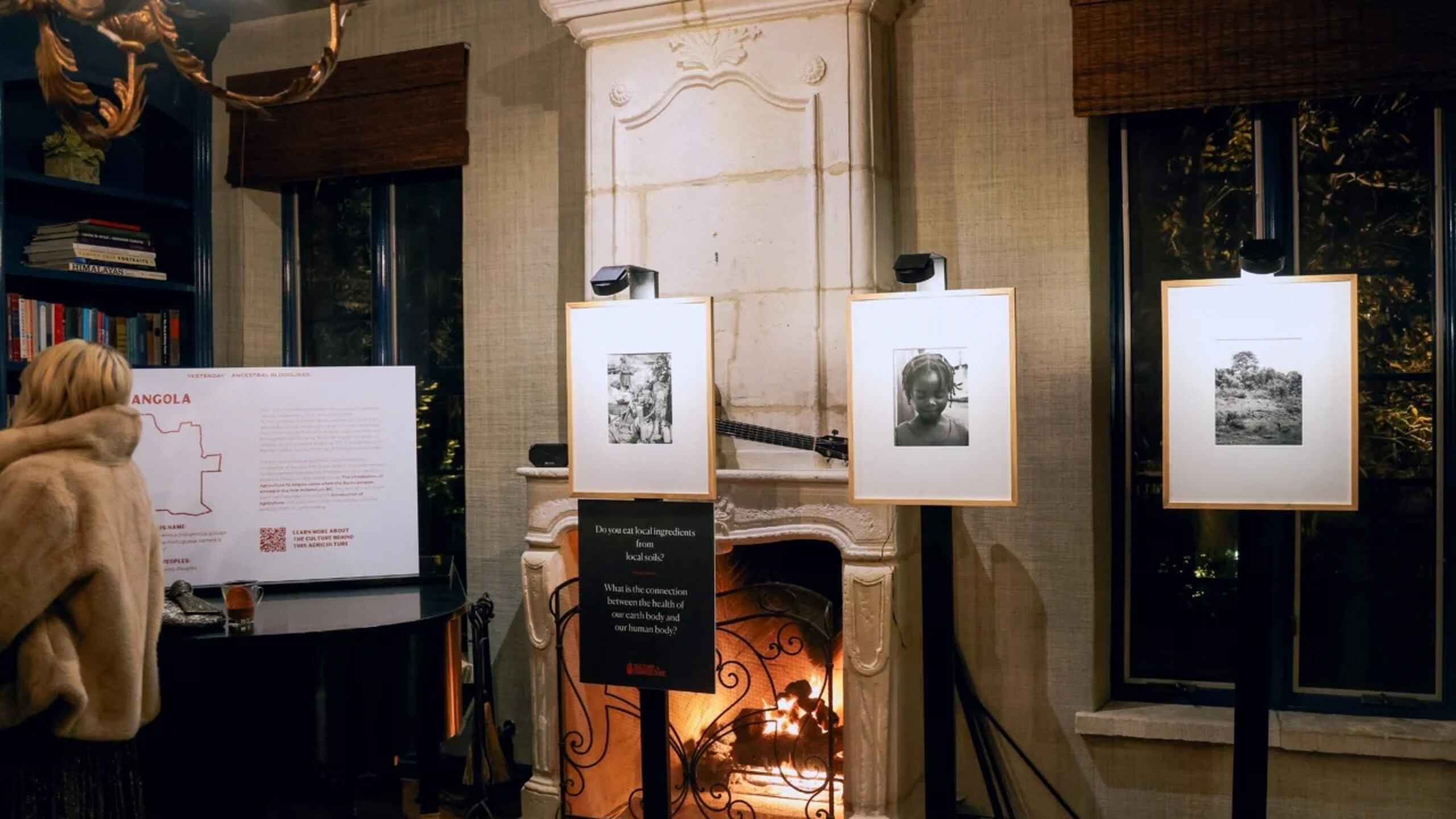 Exhibition display featuring framed photographs above a fireplace with informational panels about Angola
