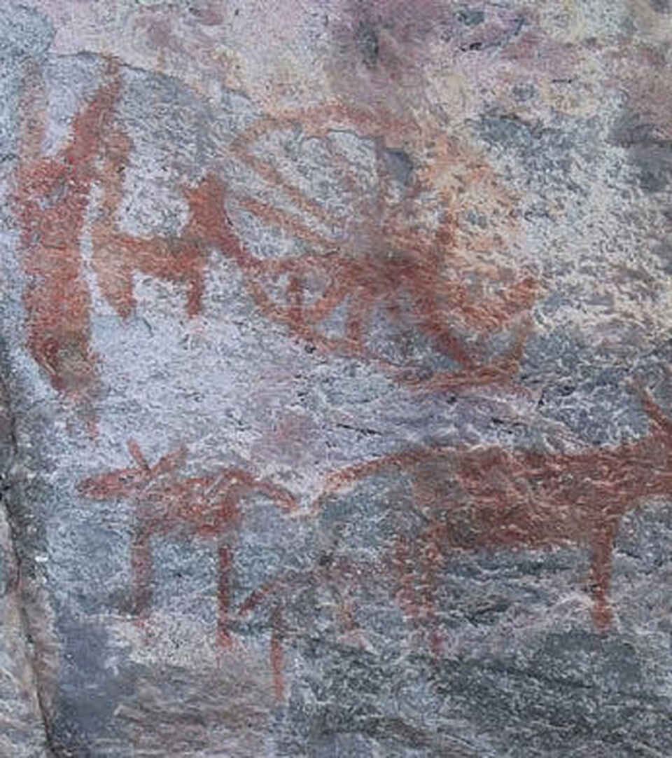 Ancient rock art depicting human and animal figures in red ochre on a stone surface